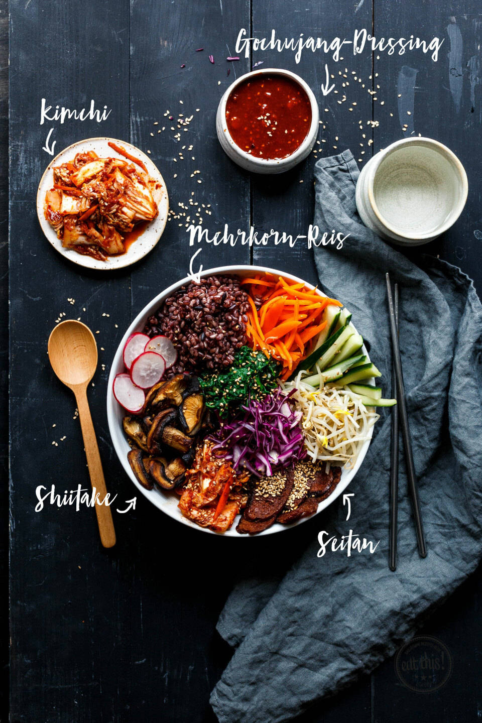 烹飪 桌布 壁紙 — 一碗色彩繽紛的韓國石鍋拌飯，配有黑米、香菇、蘿蔔和豆芽，周圍有泡菜、韓式辣醬和筷子，放在深色木桌上。