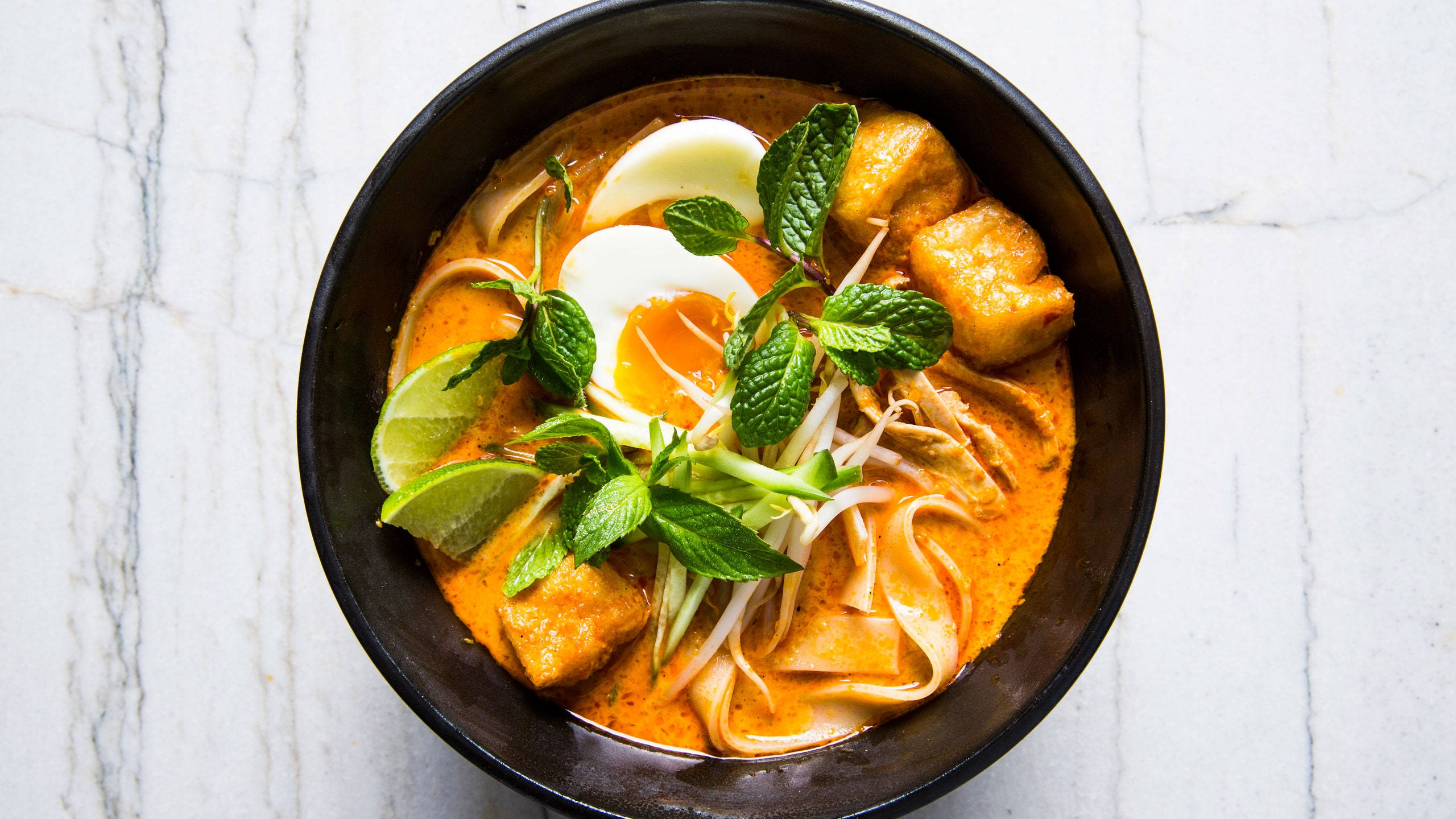 Delicious Food 桌布 壁紙 — 一碗色彩鮮豔的濃郁橙色咖哩湯麵，配上切片水煮蛋、豆芽、豆腐和新鮮薄荷，置於白色大理石表面上。