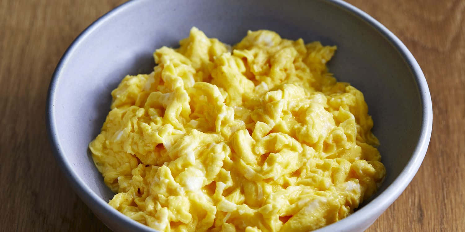 Scrambled Egg 桌布 壁紙 — 一碗蓬鬆金黃色的炒蛋放在灰色陶瓷碗中，置於溫暖的木桌上。