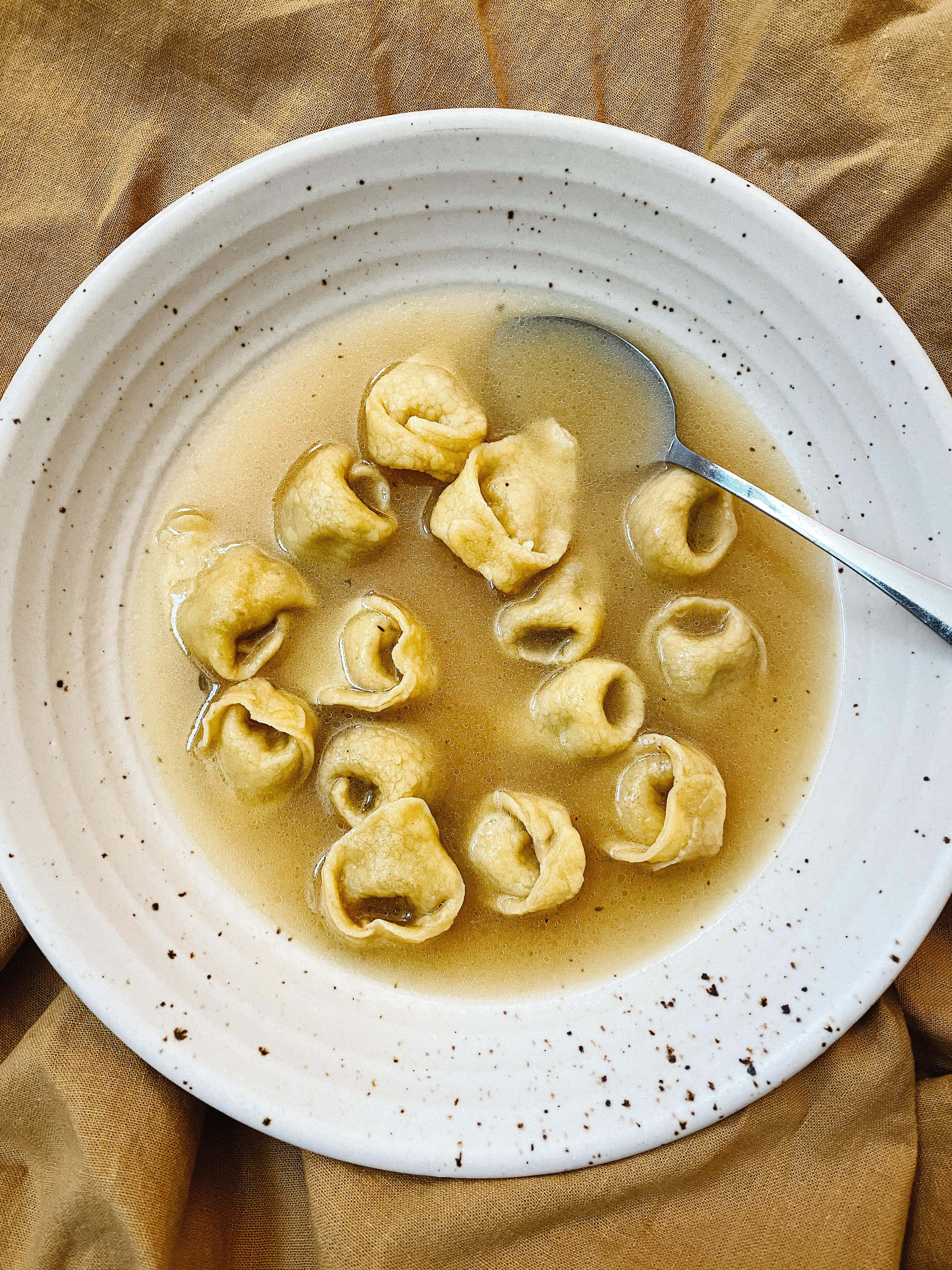 Pasta 桌布 壁紙 — 一碗鄉村風格的義大利餃子放在清湯中，置於暖色調亞麻布上，湯匙擱在碗內。