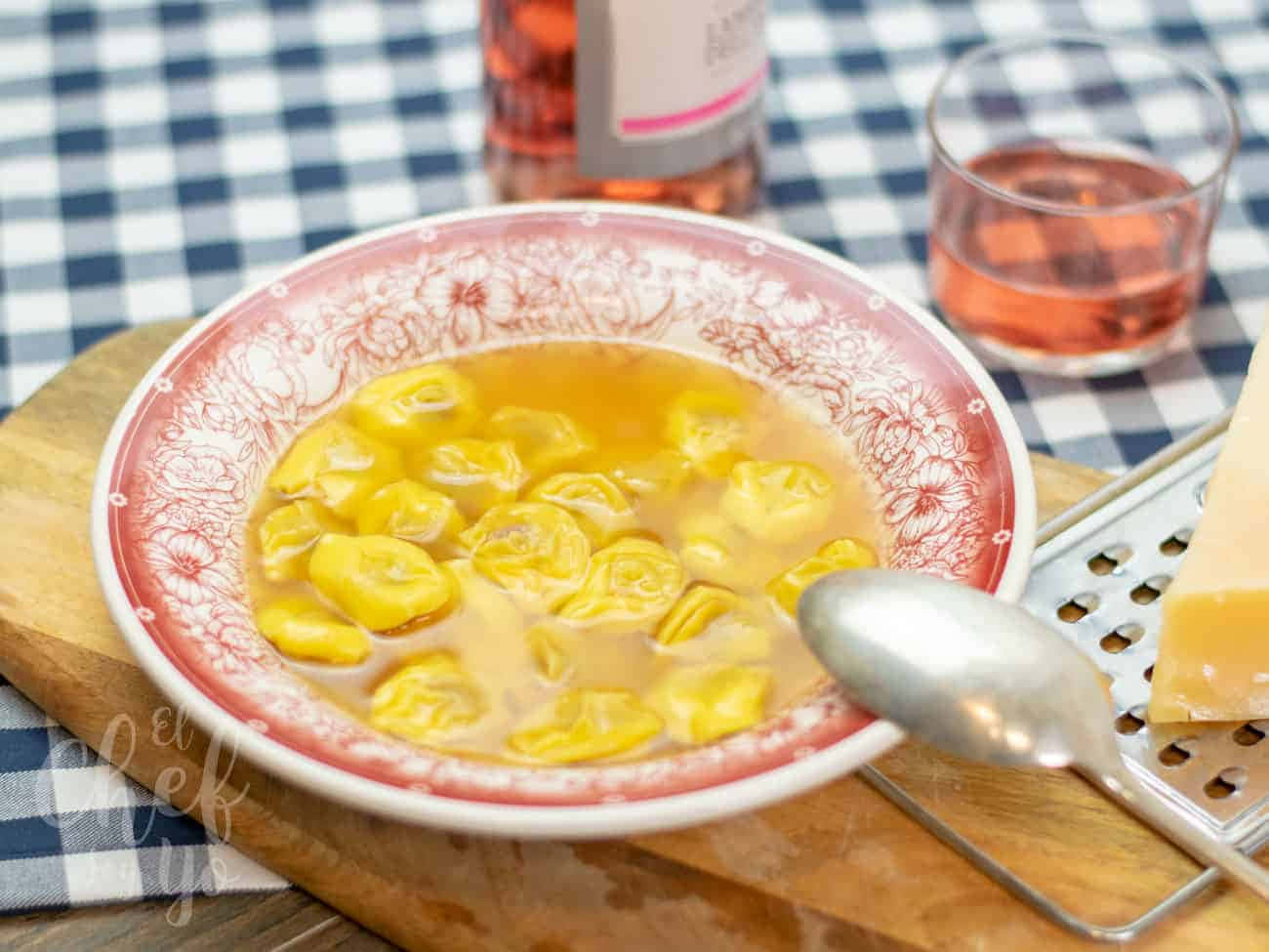 Food Photography 桌布 壁紙 — 一碗金黃色義大利餃子在湯汁中，放在木板上，旁邊有一杯玫瑰紅酒和磨碎的起司。