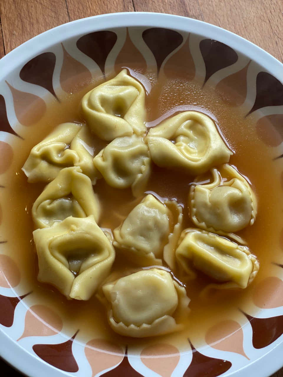 Pasta 桌布 壁紙 — 一碗金黃色餃子浮在濃湯中，放在木桌上的圖案盤子上。