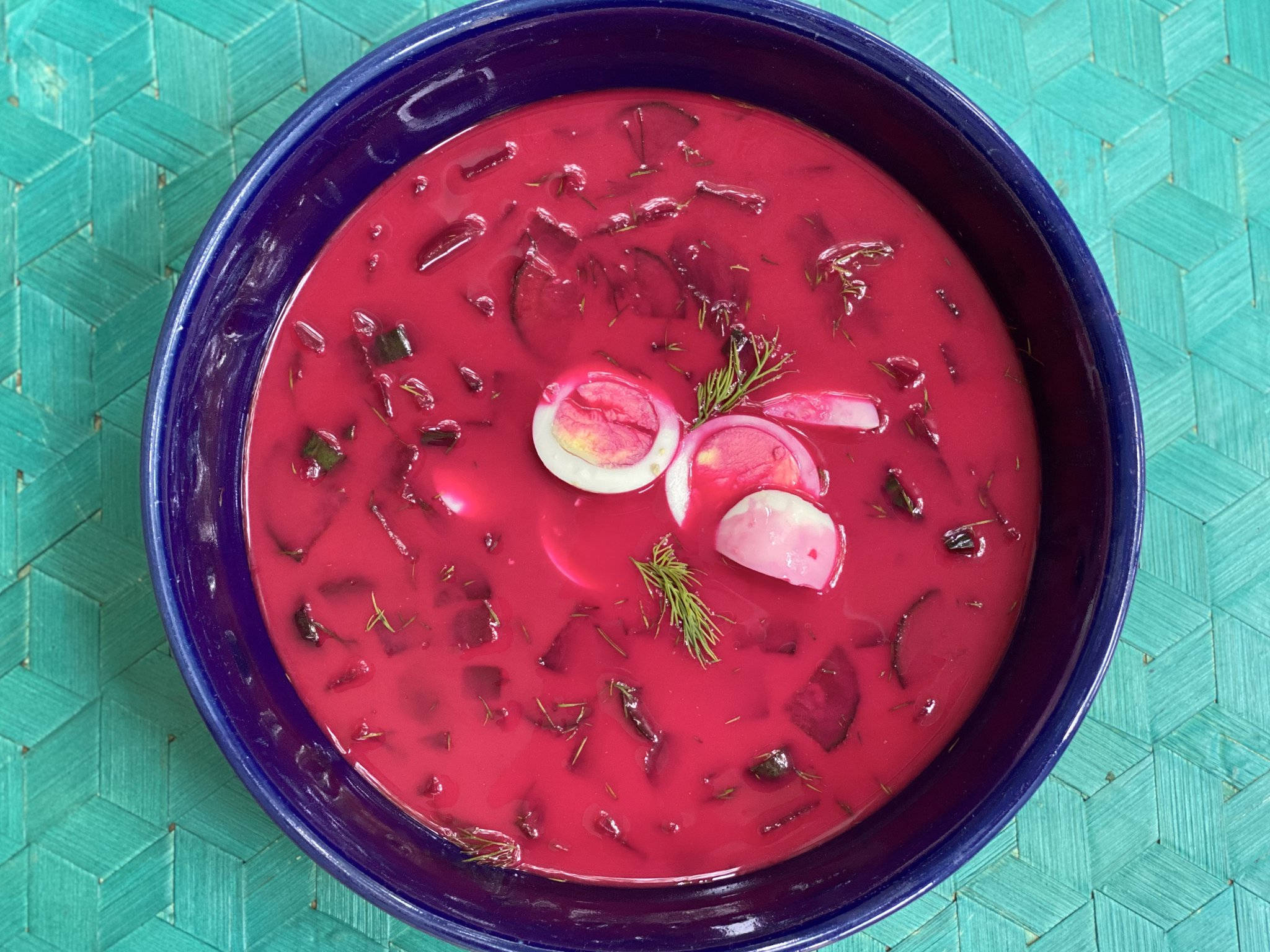 beetroot 桌布 壁紙 — 一碗鮮紅色甜菜湯盛在深藍色碗中，上面放有切片水煮蛋和新鮮蒔蘿，置於青綠色編織墊上。