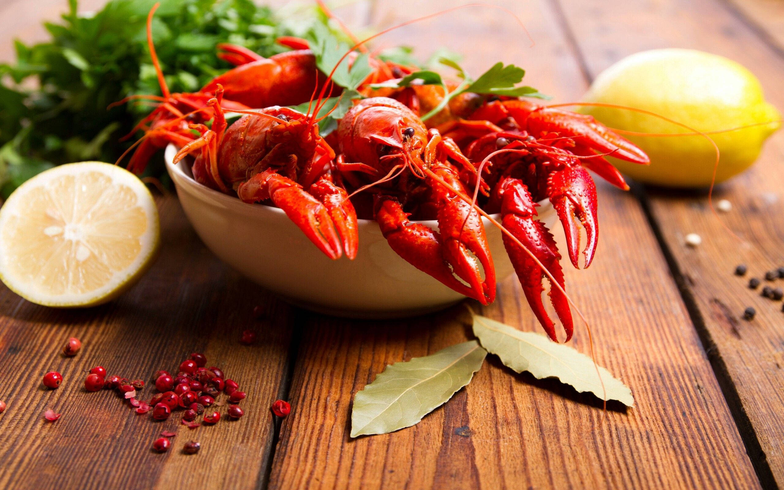 Lobster 桌布 壁紙 — 一碗鮮紅色的水煮小龍蝦，飾以歐芹、檸檬和月桂葉，放在質樸的木桌上。