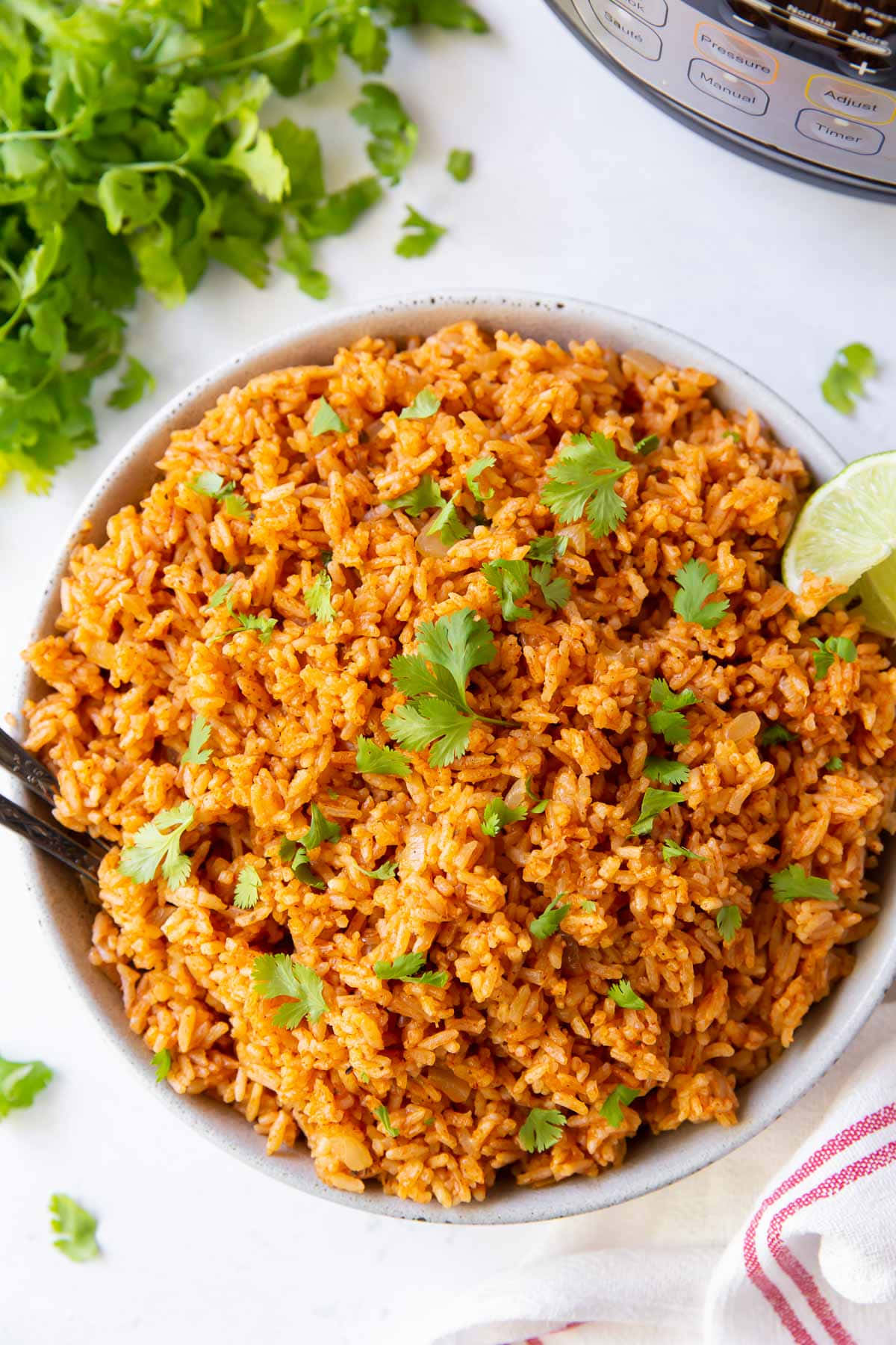 Spanish 桌布 壁紙 — 一碗鮮豔的橙色米飯，上面放著新鮮的香菜和萊姆角，旁邊有一個壓力鍋和散落的香草。