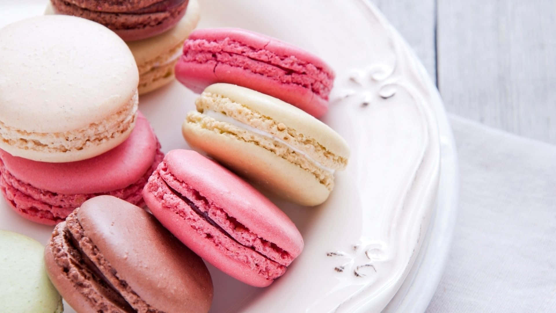 Macarons 桌布 壁紙 — 一碟色彩繽紛的馬卡龍，以柔和自然光線照射，放在白色木質表面上。