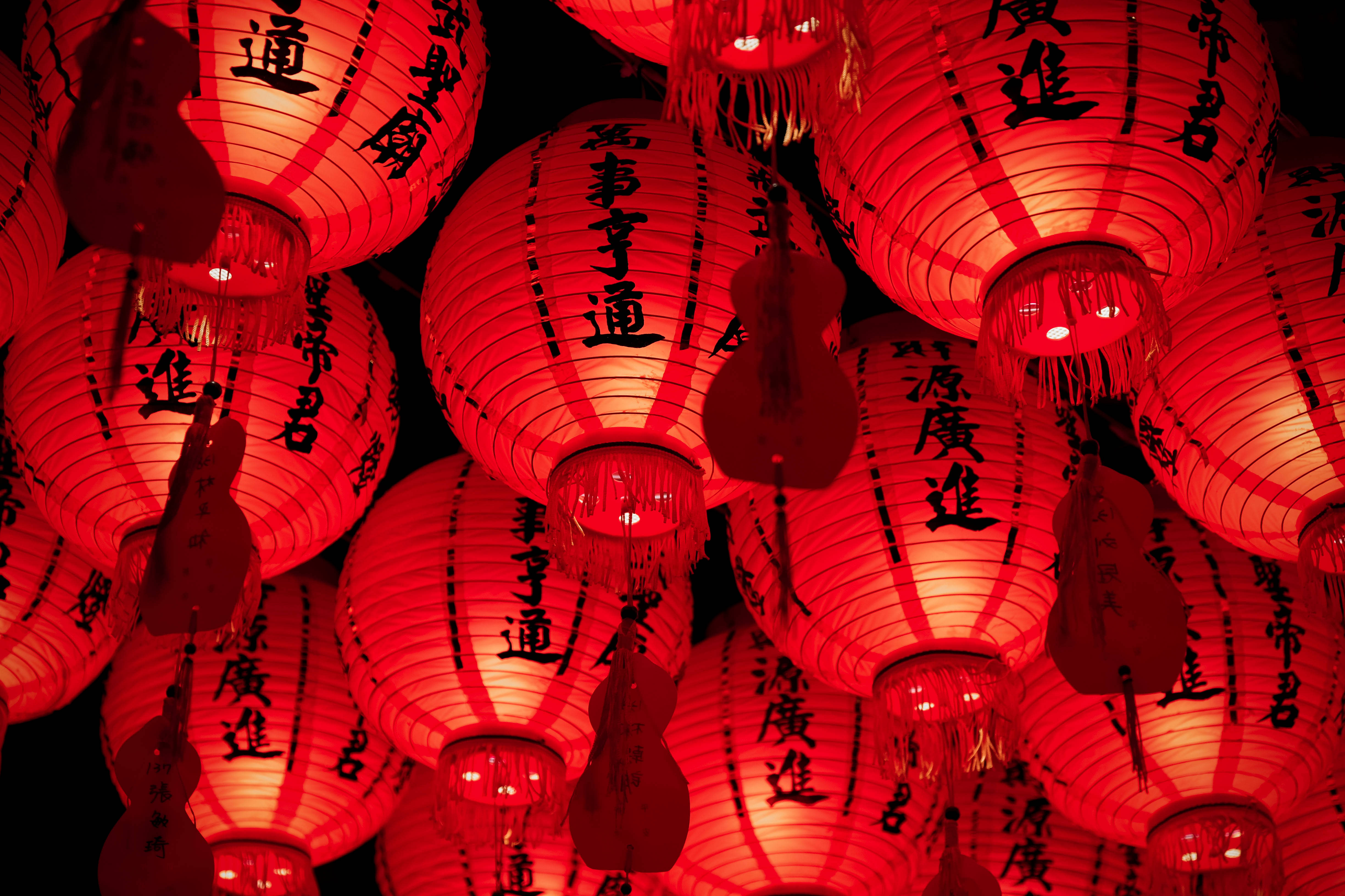 春節 桌布 壁紙 — 一簇密集的發光紅色紙燈籠，上面有黑色中文字，掛在深色背景上。