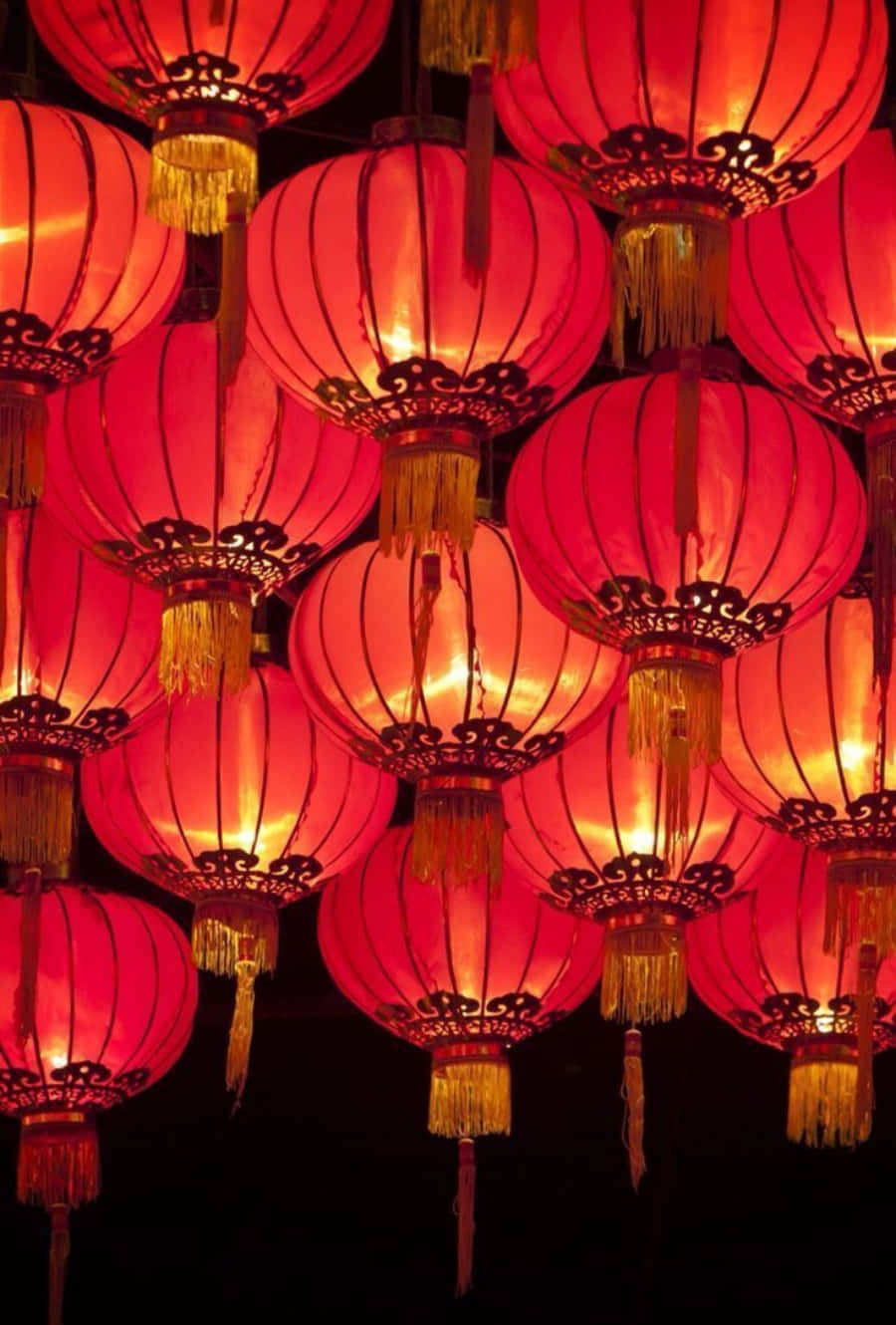 春節 桌布 壁紙 — 一簇密集的發光紅色紙燈籠，帶有金色流蘇，懸掛在黑暗的夜空中。