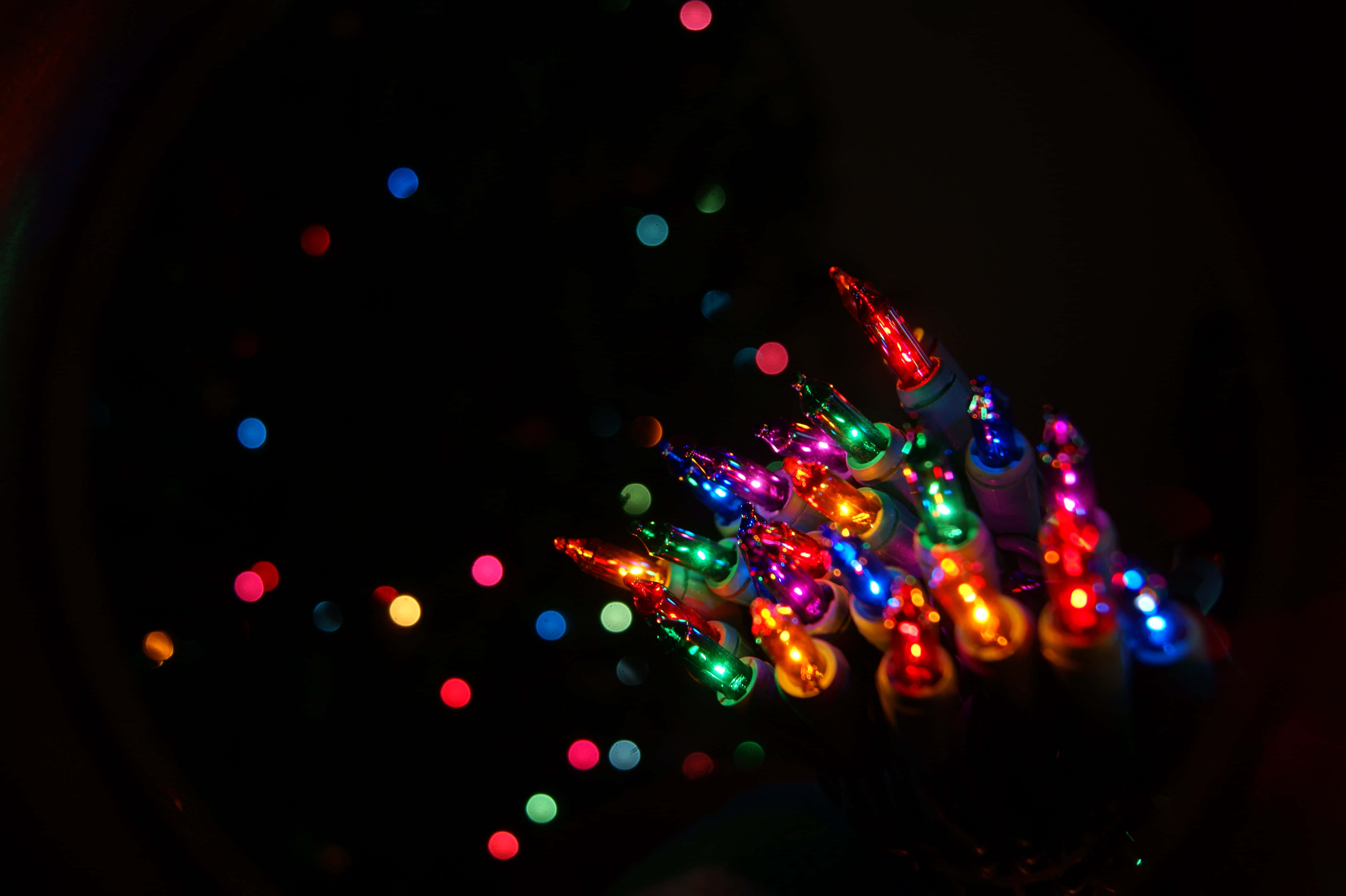 Christmas Light 桌布 壁紙 — 一簇色彩繽紛、發光的聖誕燈飾，在黑暗背景上帶有散景效果。