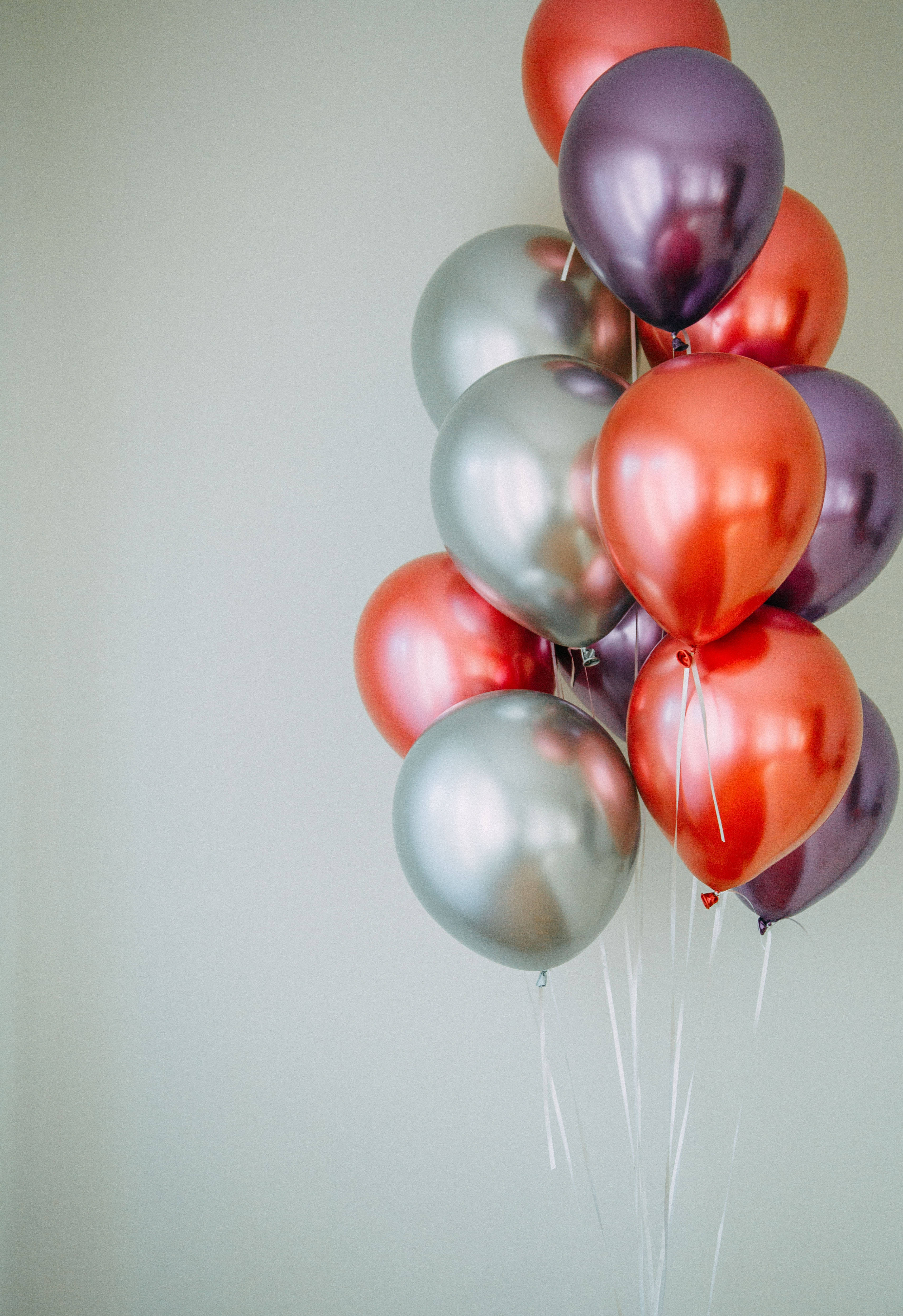 Balloons 桌布 壁紙 — 一簇閃亮的金屬氣球，紅色、銀色和紫色，漂浮在純淺灰色牆壁前。
