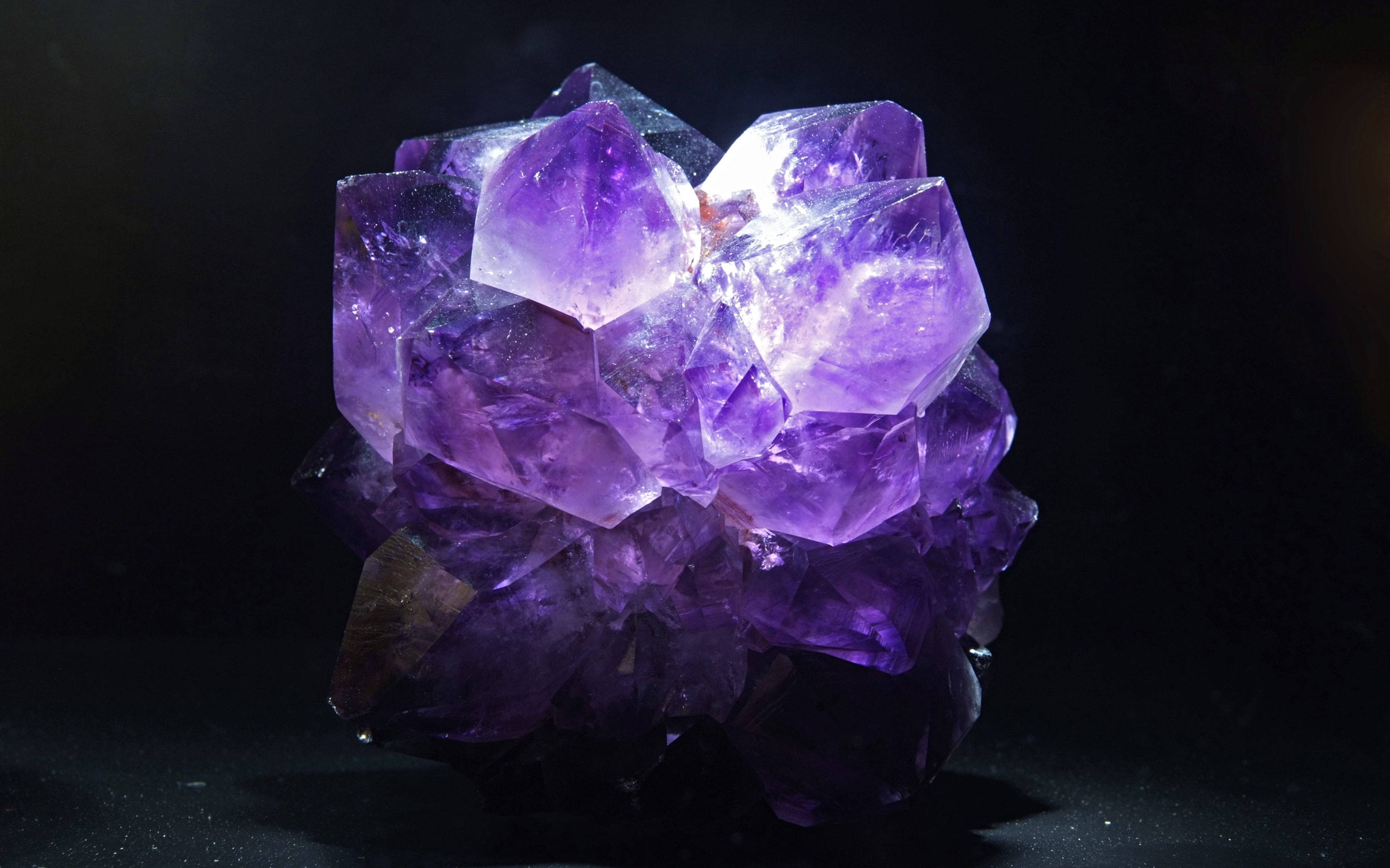 Amethyst 桌布 壁紙 — 一簇閃耀的紫色紫水晶晶體在深黑色背景下發出內在光芒。