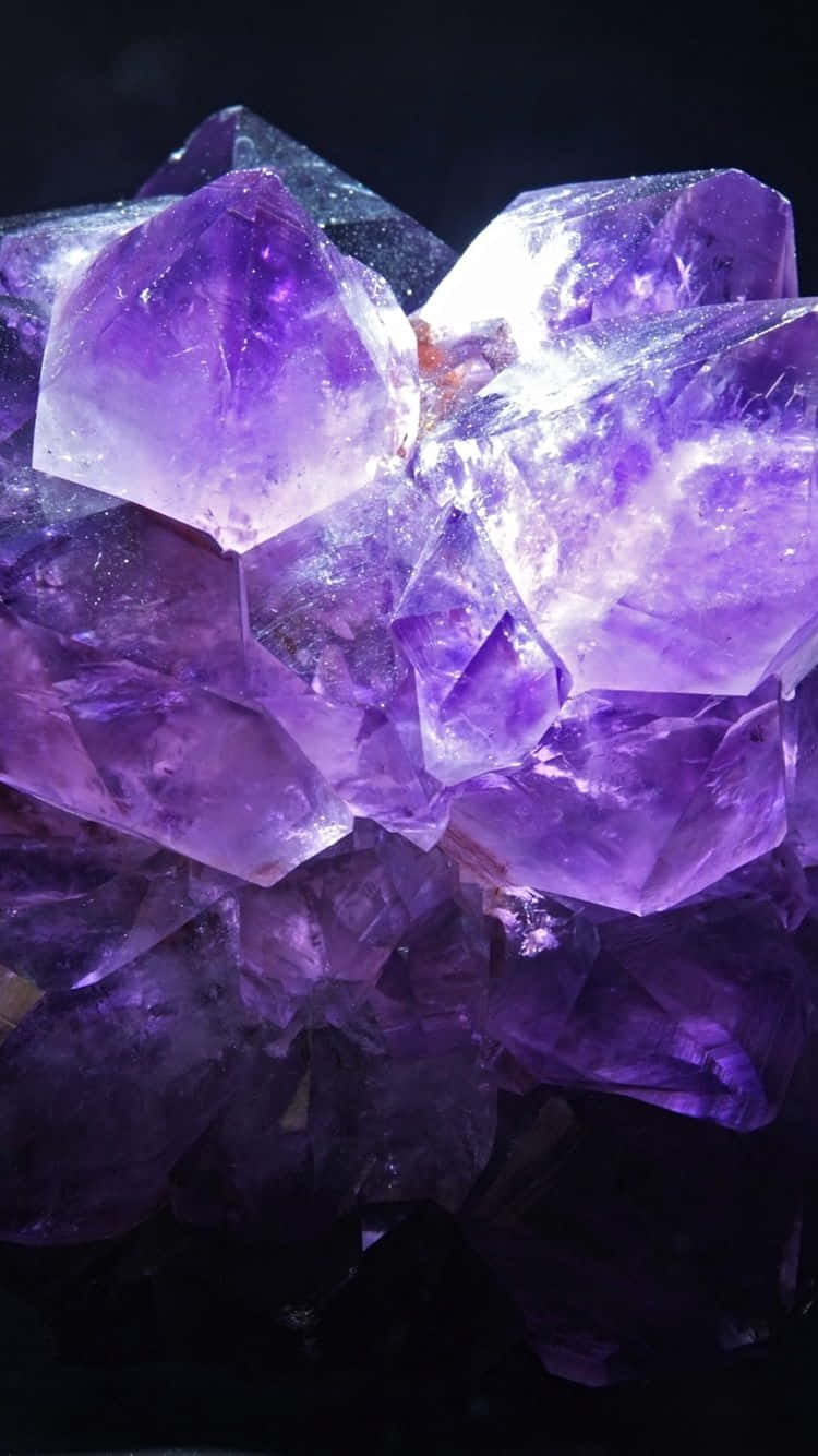 紫水晶 桌布 壁紙 — 一簇閃耀的紫色紫水晶晶體在聚焦光線下，在深黑色背景上閃閃發光。