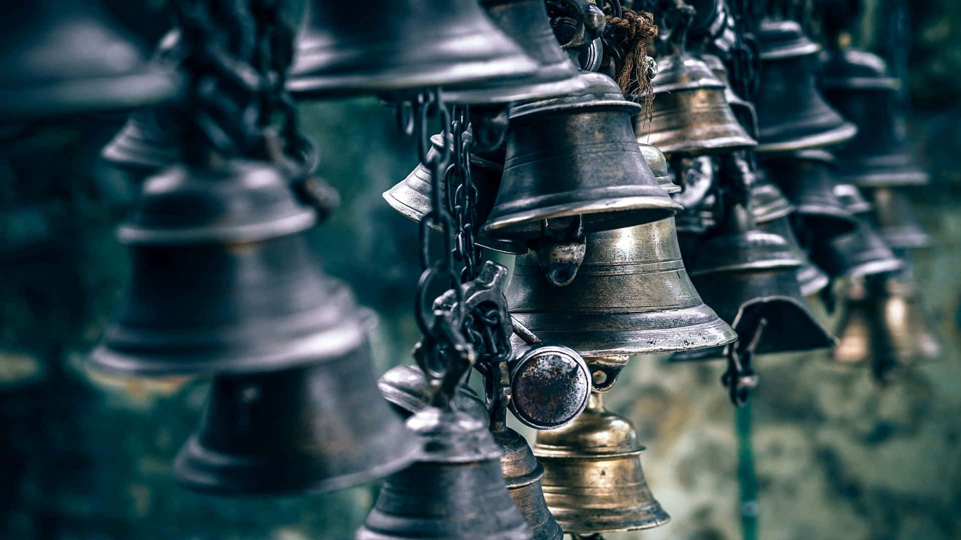 Bell 桌布 壁紙 — 一簇風化的金屬鐘用鏈條懸掛在模糊的綠色背景上。