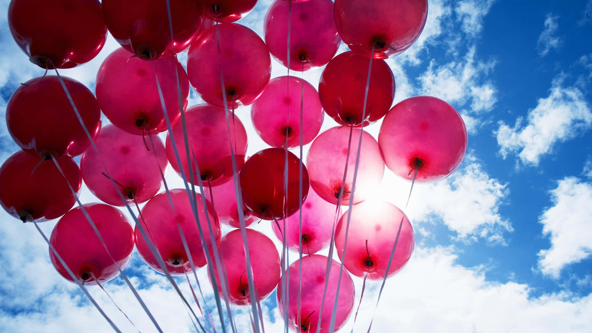 Balloon 桌布 壁紙 — 一簇鮮豔的粉紅色和紅色氣球在明亮的藍天中飄浮，伴隨著蓬鬆的白雲。