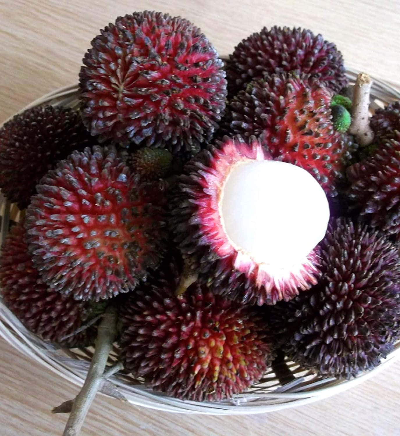 Rambutan 桌布 壁紙 — 一籃帶刺的紅色紅毛丹，其中一個裂開露出奶油白色的果肉。