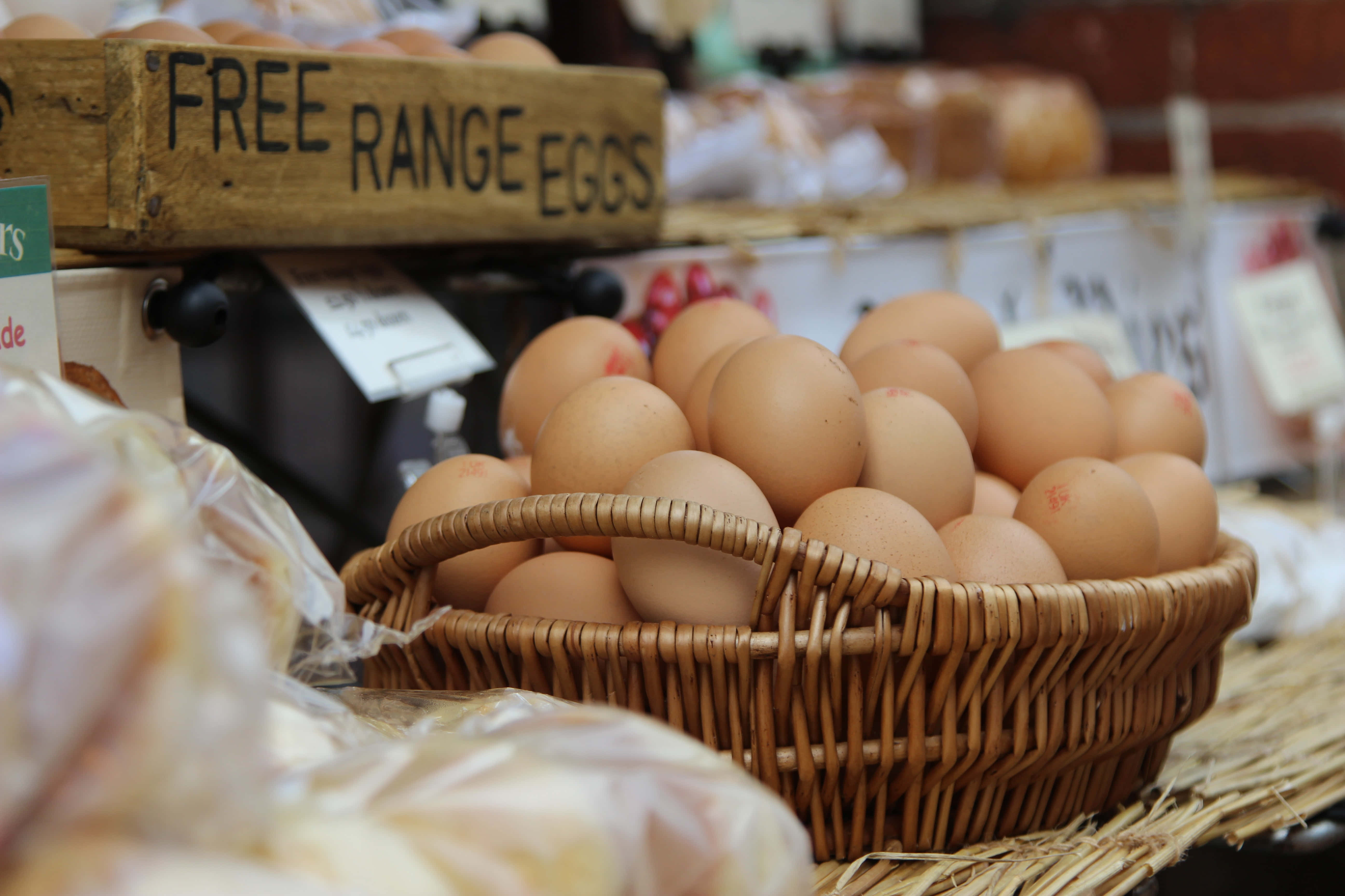 Brown Eggs 桌布 壁紙 — 一籃棕色放養雞蛋放在一個市場攤位上，上方有一個木牌。
