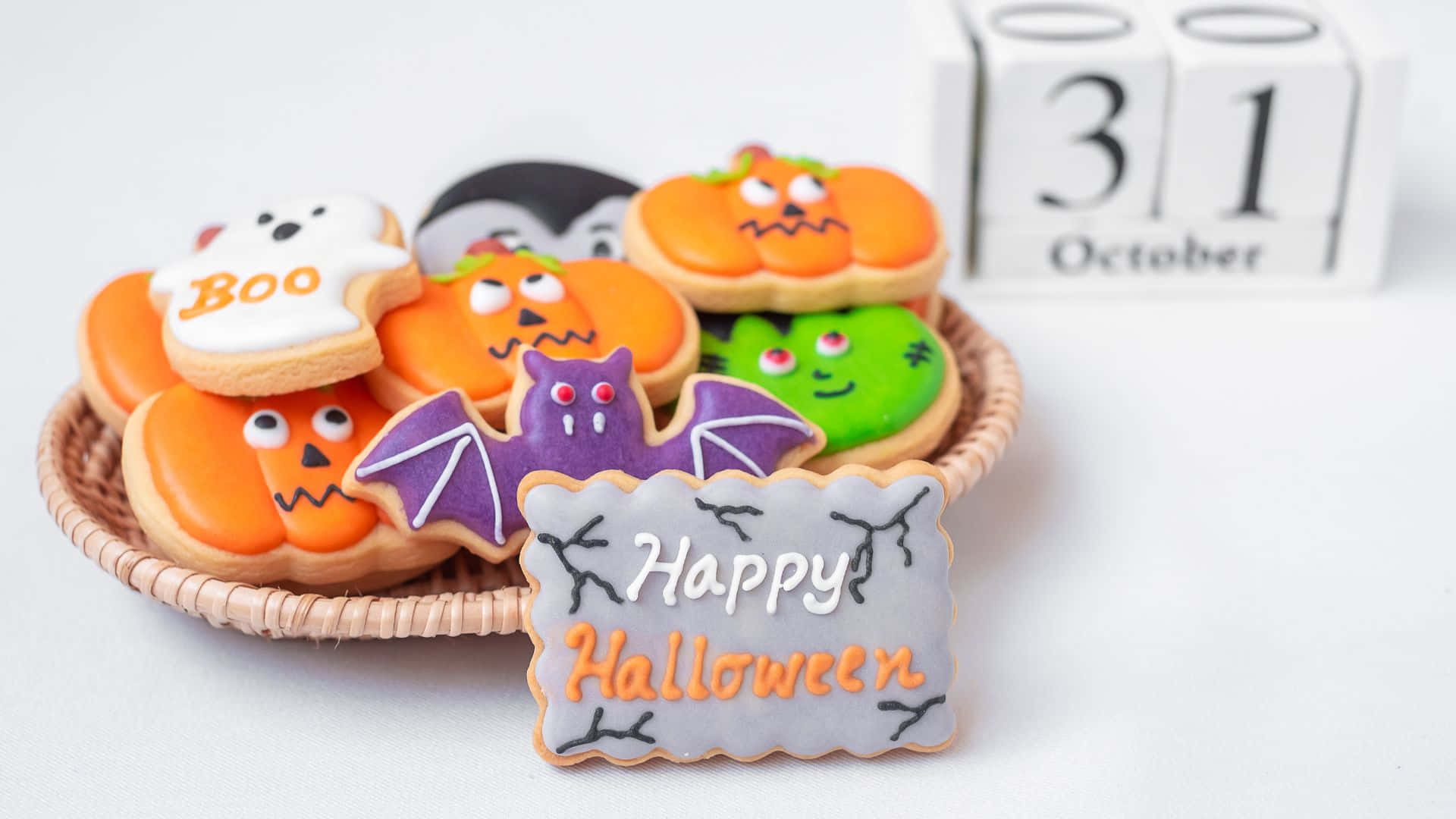 October 31st 桌布 壁紙 — 一籃色彩繽紛的萬聖節主題糖餅乾，形狀包括南瓜、鬼魂、蝙蝠和吸血鬼，附有'Happy Halloween'標誌和顯示10月31日的日曆。