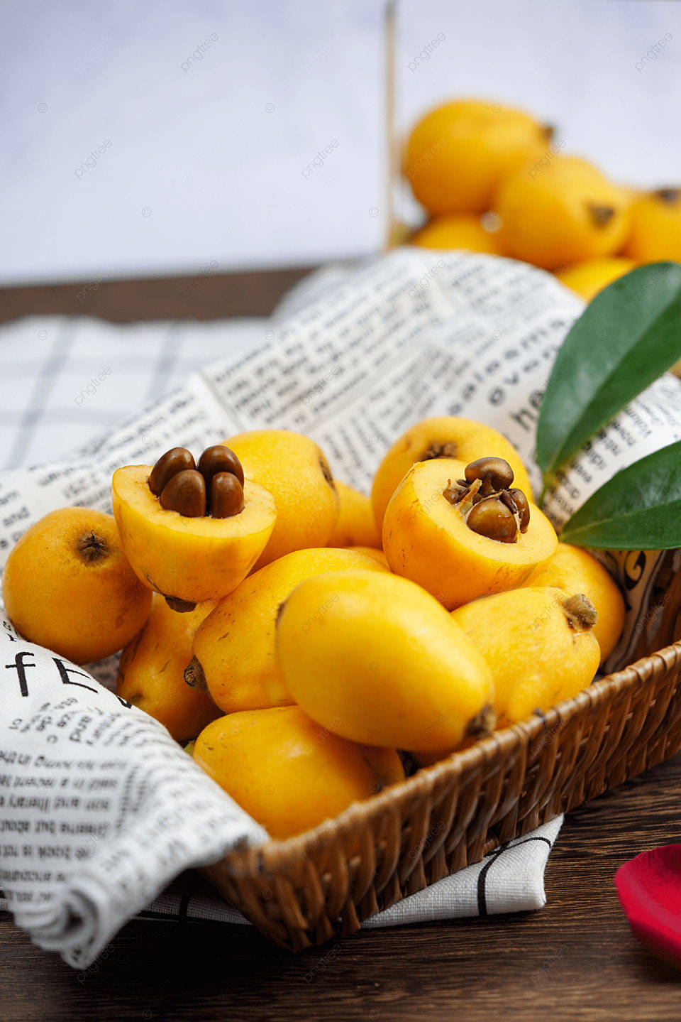 Fruits 桌布 壁紙 — 一籃鮮黃色的枇杷，帶有深色種子和光澤綠葉，放在木桌上的報紙上。