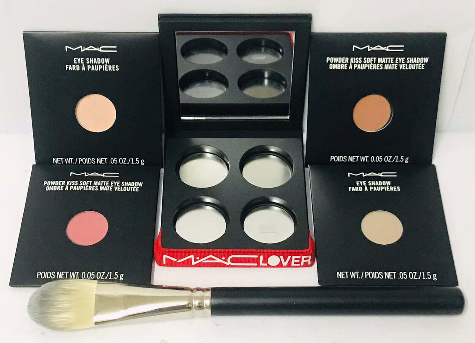 Mac Cosmetics 桌布 壁紙 — 一系列MAC化妝品，包括霧面眼影和一把蓬鬆的刷子，整齊地擺放在白色表面上。