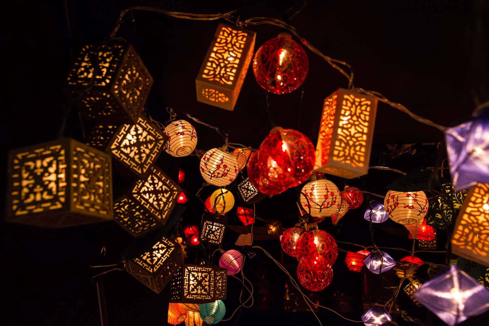 Lantern 桌布 壁紙 — 一系列令人眼花撩亂的發光燈籠，帶有精緻的鏤空和鮮豔的色彩，懸掛在黑暗的夜空中。