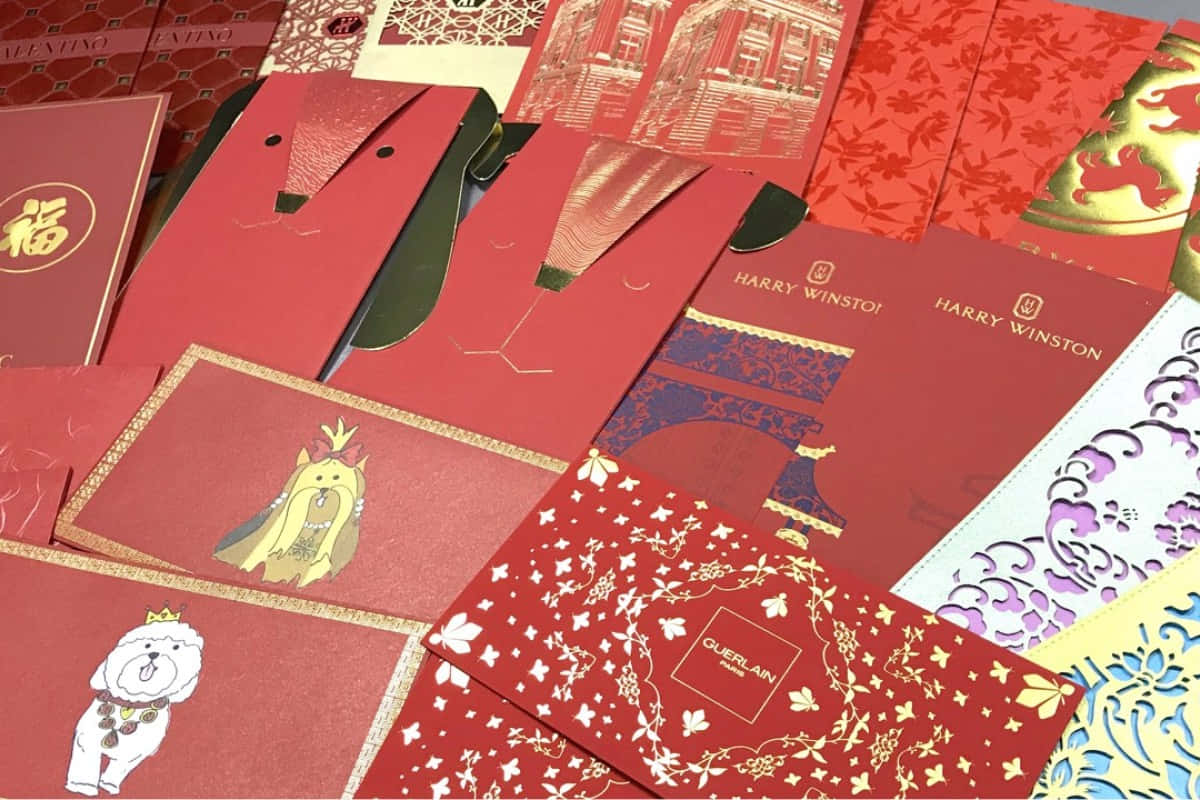 Red Envelope 桌布 壁紙 — 一系列充滿活力的奢華紅色信封，飾有金色箔紙設計，包含狗、皇冠和品牌標誌。