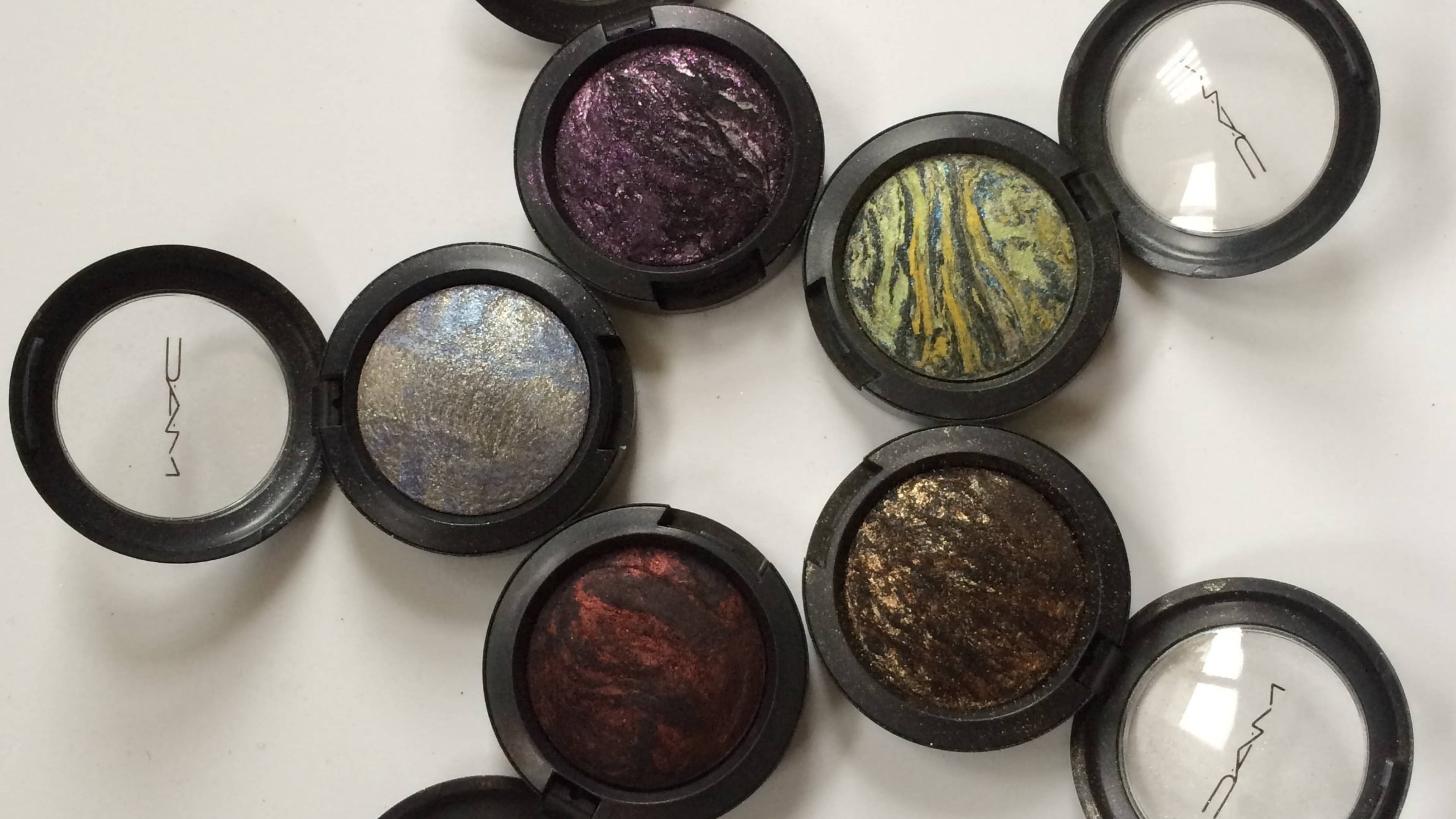 Cosmetics 桌布 壁紙 — 一系列打開的MAC眼影盤，在潔白表面上展示充滿活力的金屬色和雲石紋色調。