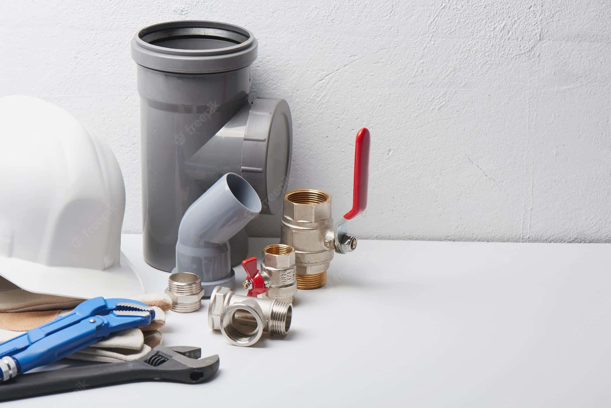Plumbing 桌布 壁紙 — 一系列水管工具和管道整齊地排列在白色表面上，背景為有紋理的牆壁。