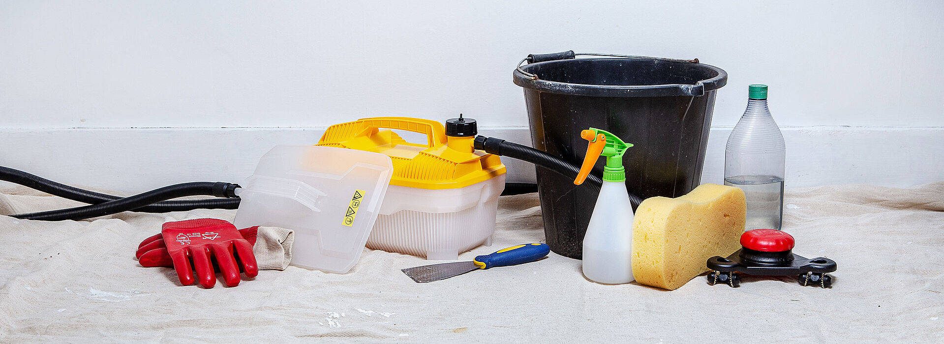 Cleaning 桌布 壁紙 — 一系列清潔工具，包括手套、海綿、噴霧瓶和水桶，排列在防護布上，背景為素牆。