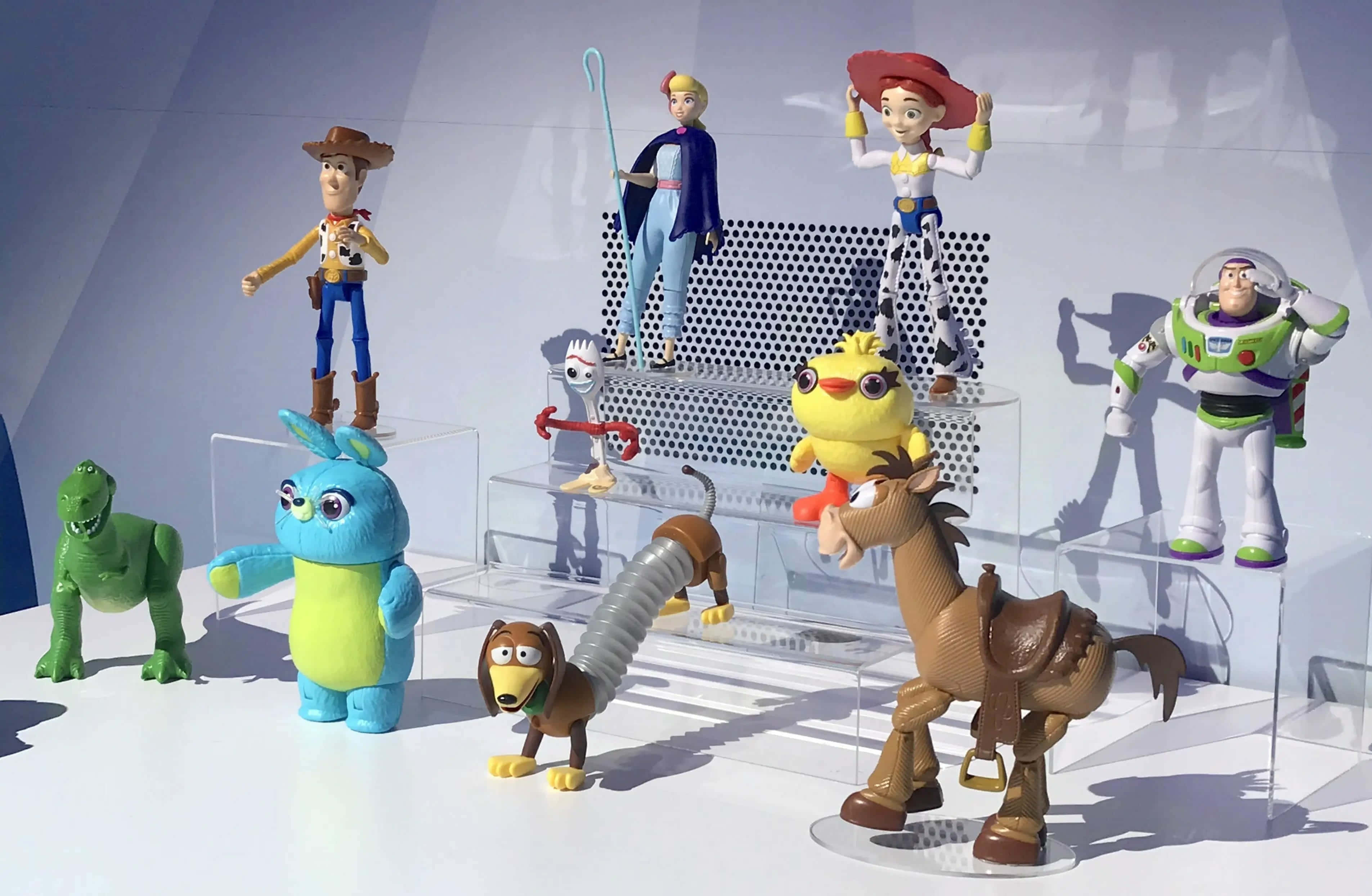 Toy Story 4 桌布 壁紙 — 一系列色彩繽紛的《玩具總動員》人偶，以透明壓克力支架展示在簡約白色背景上。