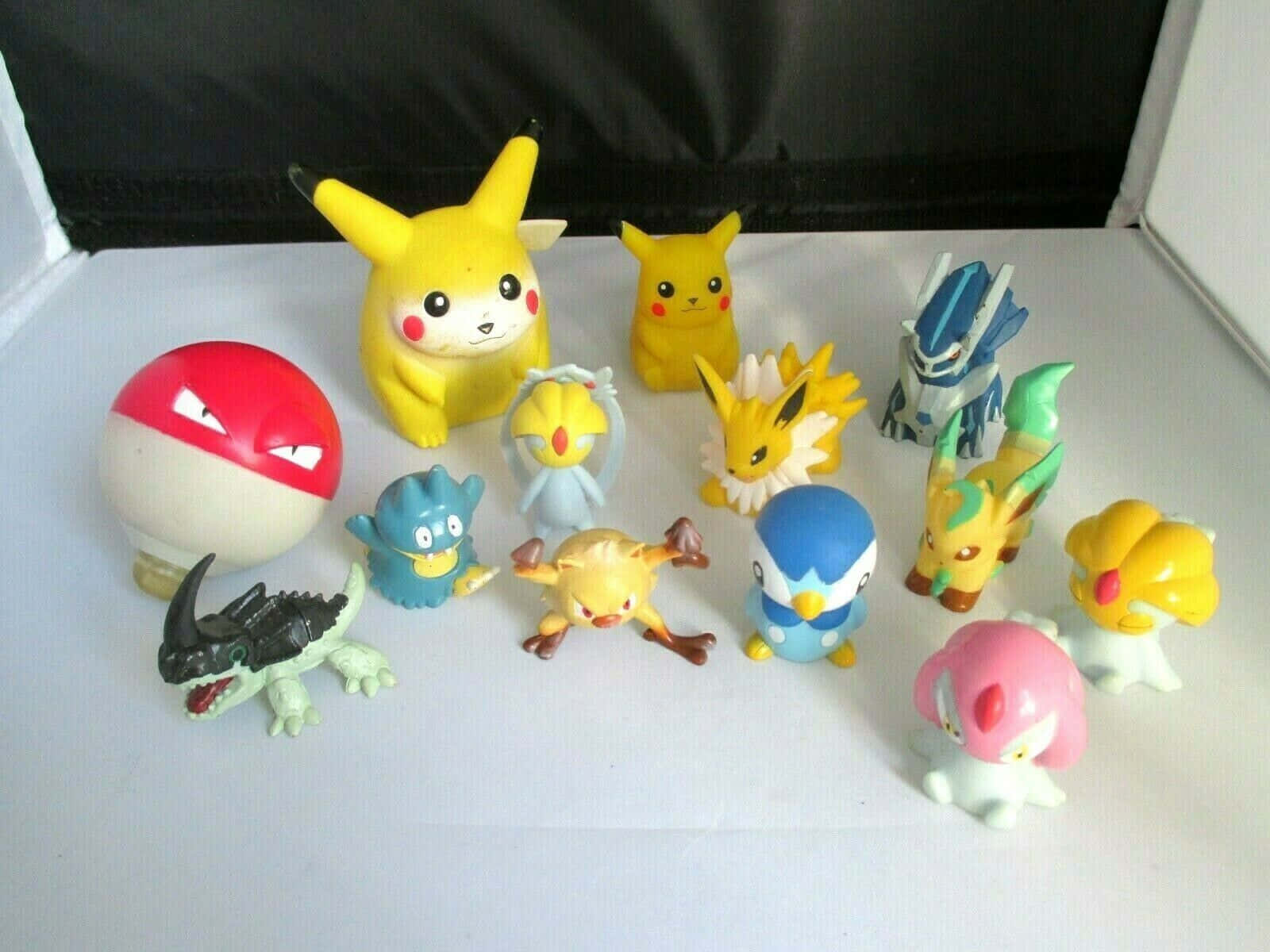 Pokemon Figures 桌布 壁紙 — 一系列色彩繽紛的寶可夢公仔和一個寶可夢球排列在白色表面上，背景為黑色。
