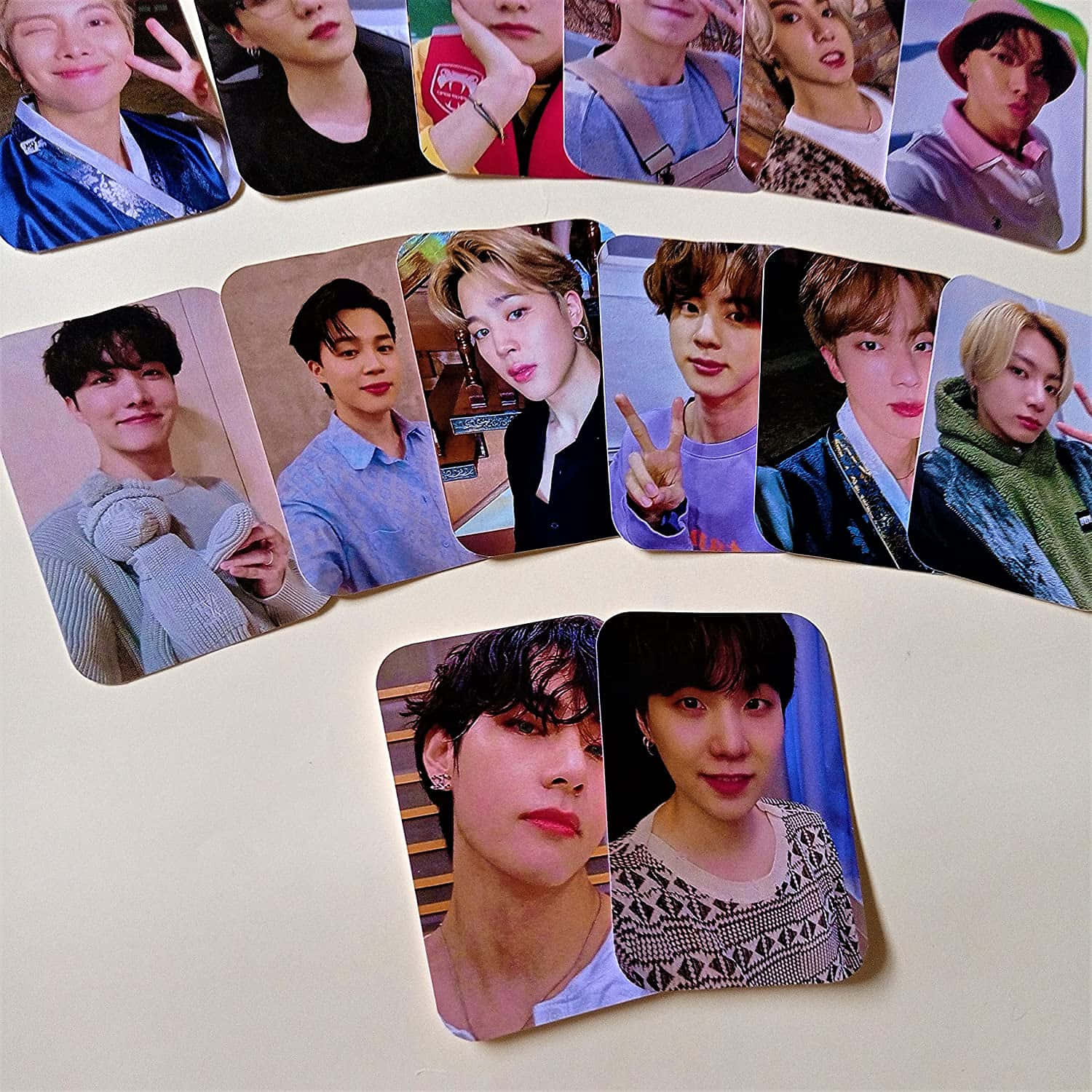 BTS 桌布 壁紙 — 一系列色彩繽紛的年輕男性肖像照片，表情和服裝各異，散落在純米白色表面上。