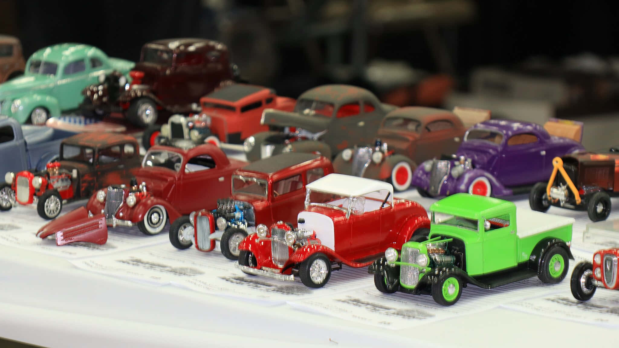 Car Model 桌布 壁紙 — 一系列色彩鮮豔的復古熱棒模型車，採用大膽的顏色如紅色、綠色和紫色，展示在白色表面上。