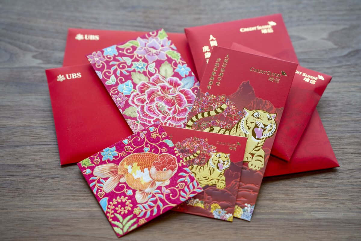 Red Envelope 桌布 壁紙 — 一系列色彩鮮豔的紅色和粉紅色中國新年紅包，帶有金色老虎、魚和花卉圖案，放置在木質表面上。