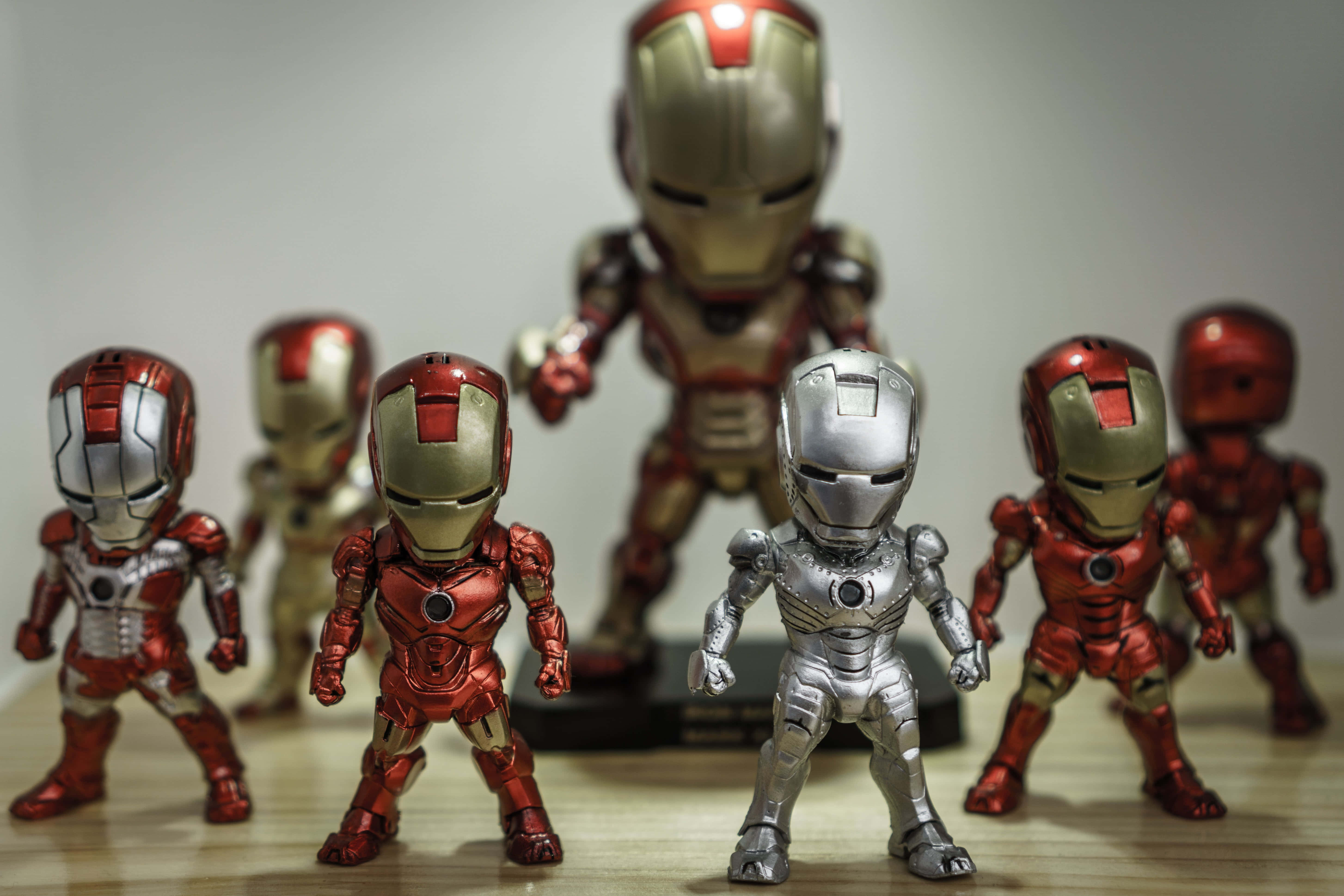 Iron Man Action Figures 桌布 壁紙 — 一系列身穿紅色、金色和銀色盔甲的鋼鐵人動作人偶，在柔和的工作室燈光下擺放在木質表面上。