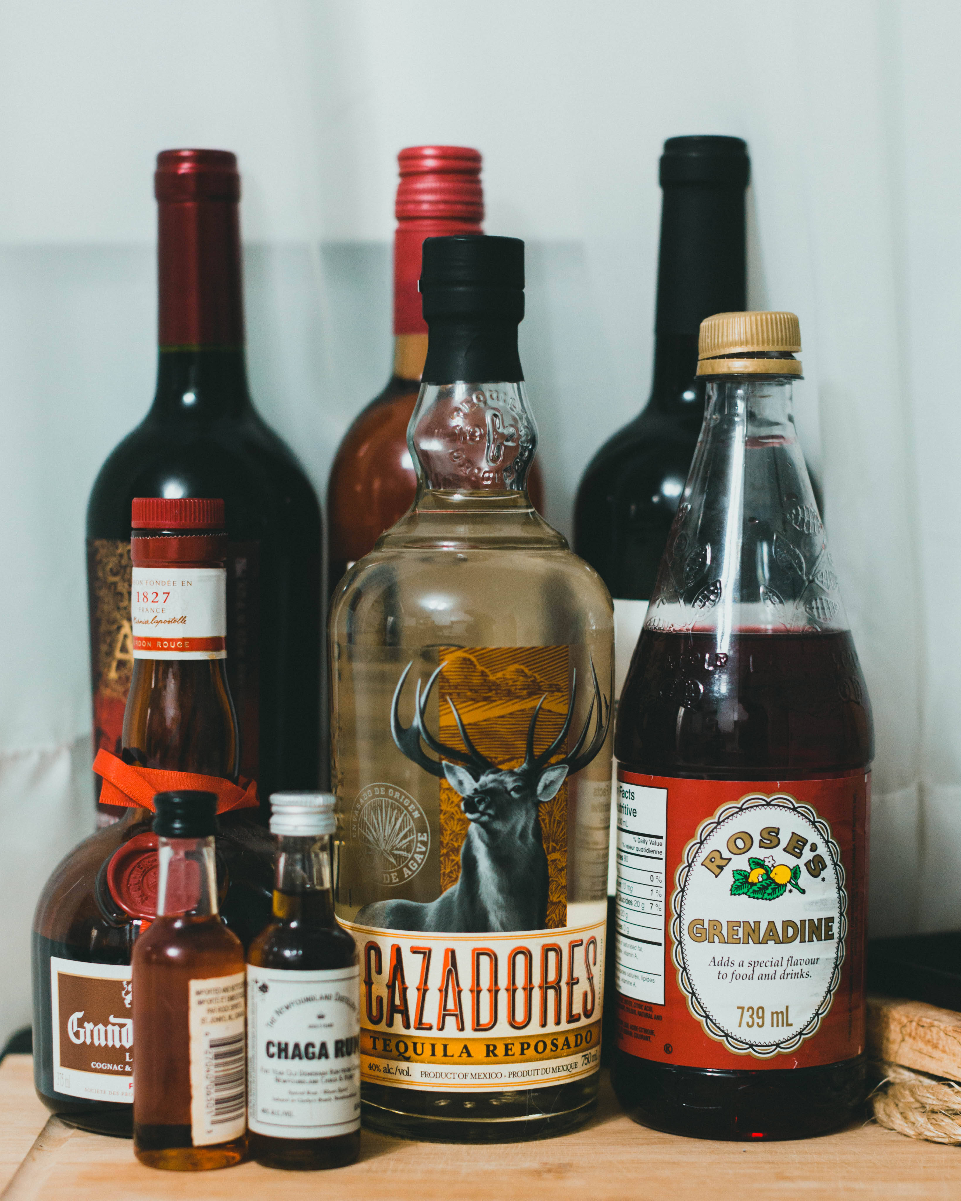 alcohol 桌布 壁紙 — 一系列酒瓶，包括龍舌蘭和石榴糖漿，排列在木質表面上，背景為白色。