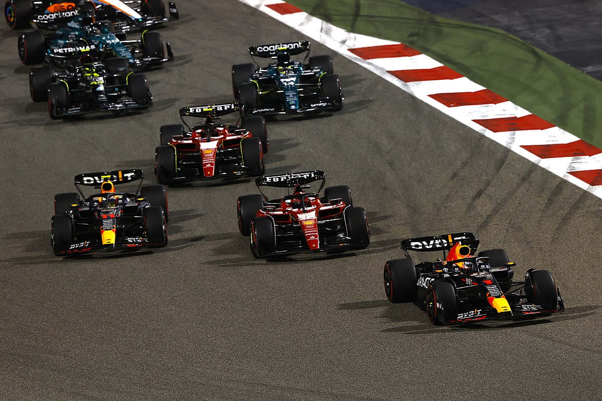 F1 桌布 壁紙 — 一級方程式賽車在夜間濕滑的賽道上緊密競賽，紅色和白色的路肩清晰可見。