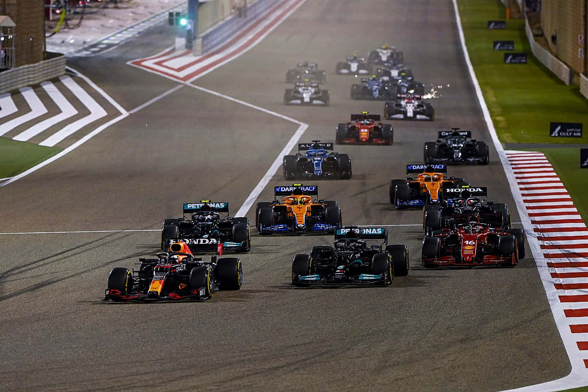 F1 桌布 壁紙 — 一級方程式賽車在夜間緊密地比賽，在明亮照明的瀝青賽道上，帶有紅色和白色的路緣石。
