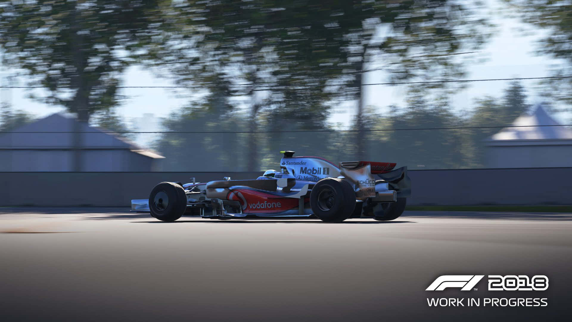 race car 桌布 壁紙 — 一級方程式賽車在賽道上疾馳，背景是模糊的樹木和建築物。