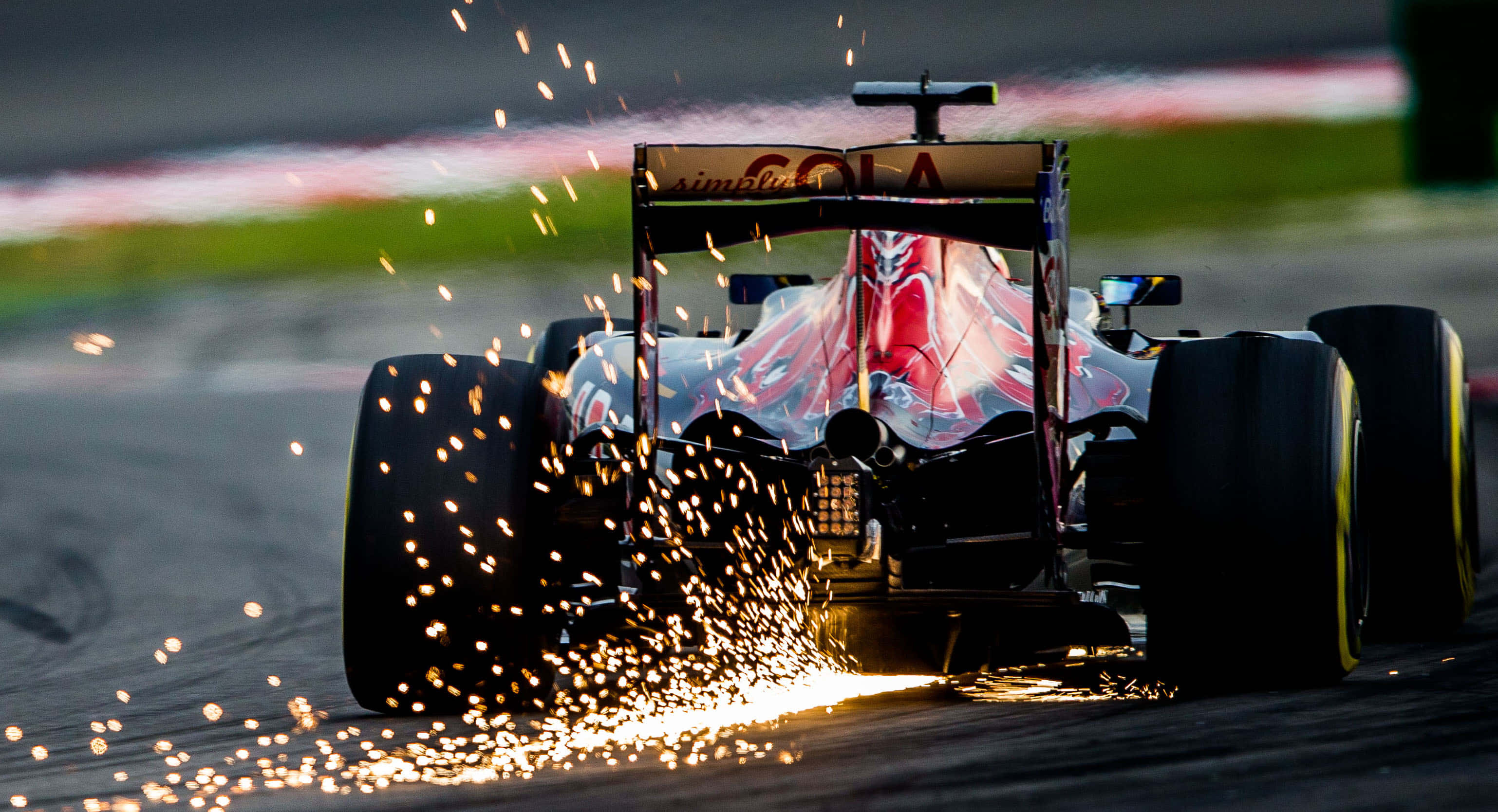 HD F1 2016 桌布 壁紙 — 一級方程式賽車在賽道上高速奔馳，輪胎擦出火花，背景模糊。