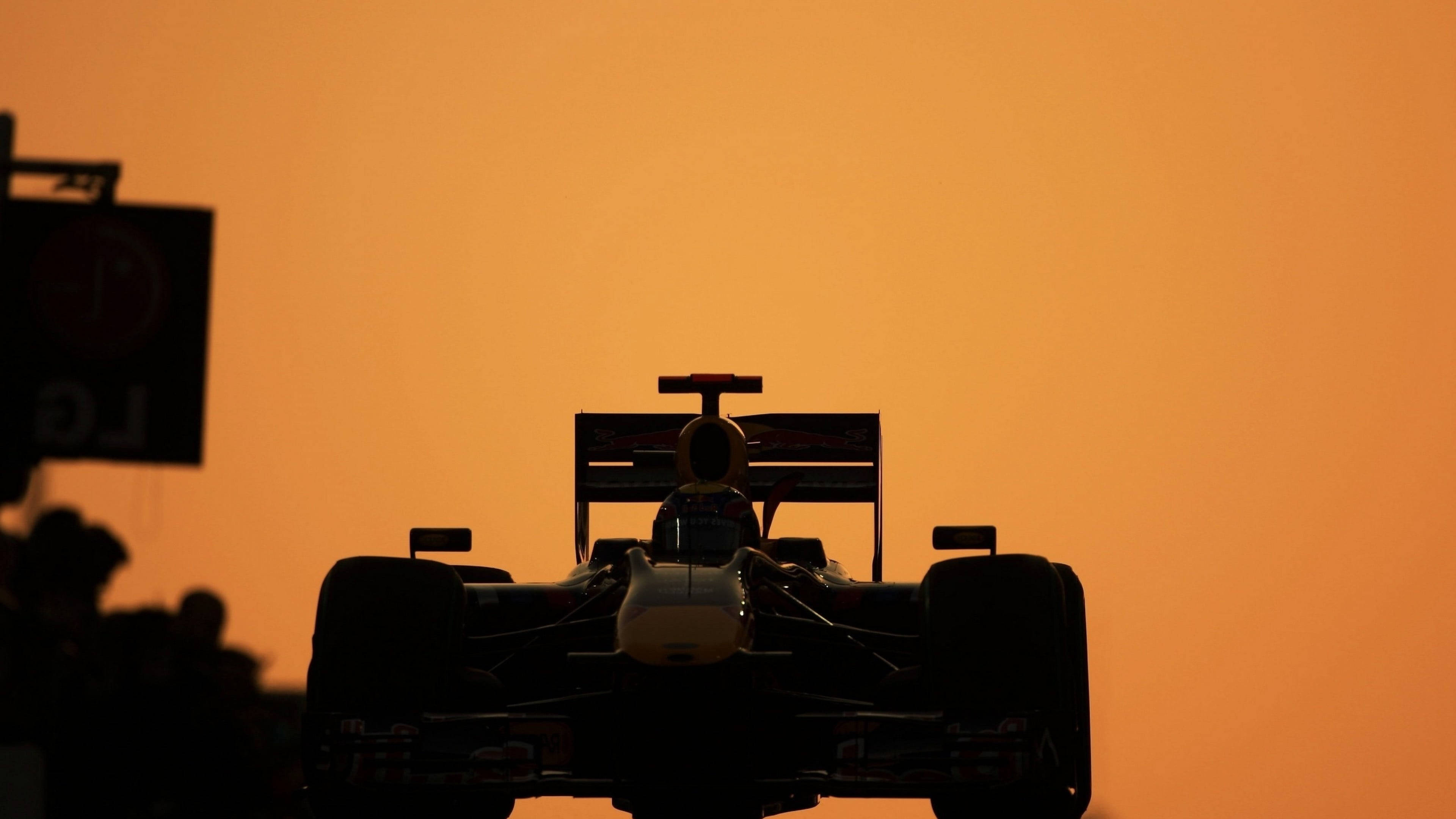 F1 桌布 壁紙 — 一級方程式賽車的剪影，背景是充滿活力的橙色日落天空，還有模糊的觀眾。