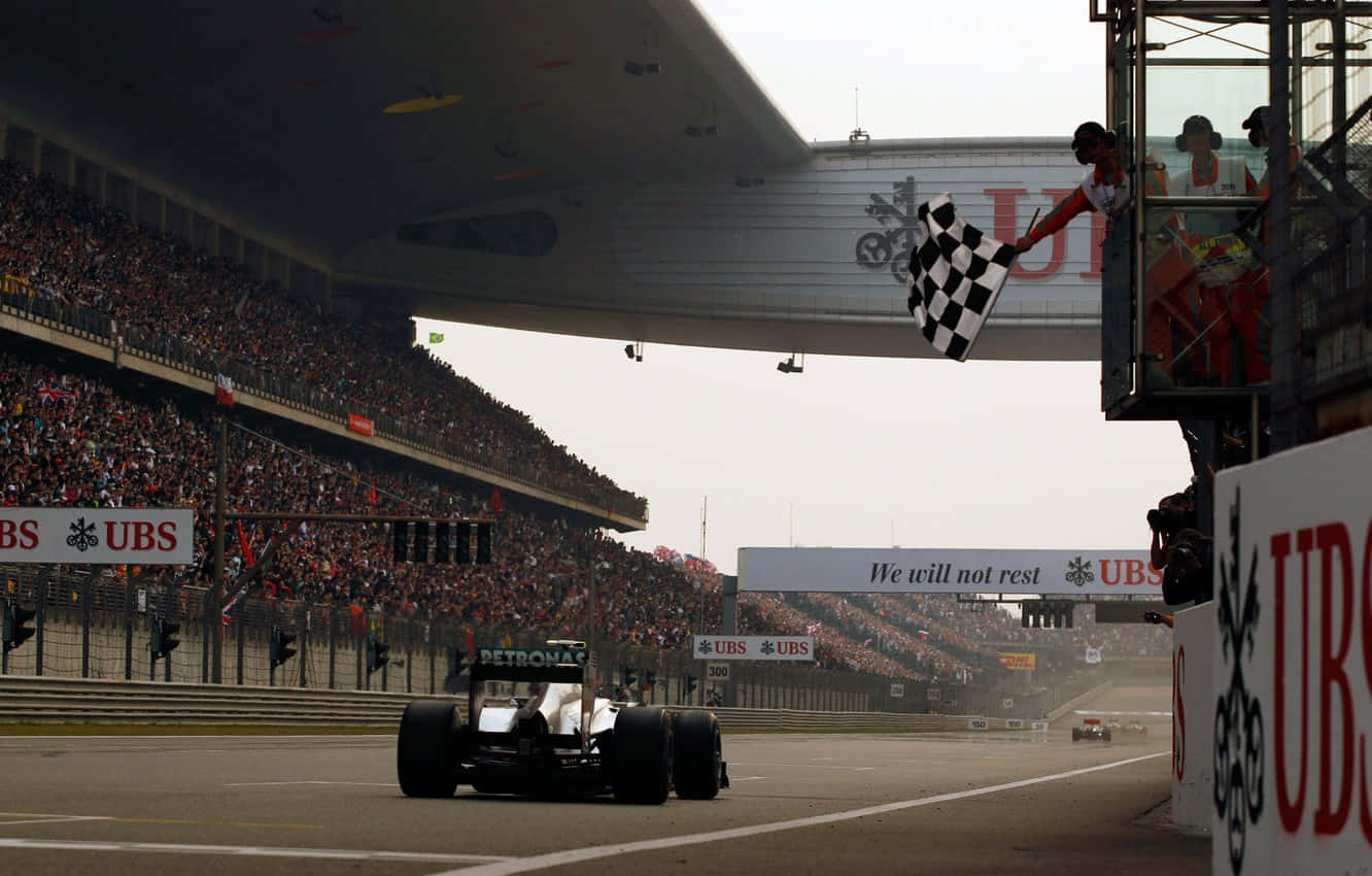 Race Track 桌布 壁紙 — 一級方程式賽車越過終點線，方格旗在擠滿觀眾的看台上方揮舞。