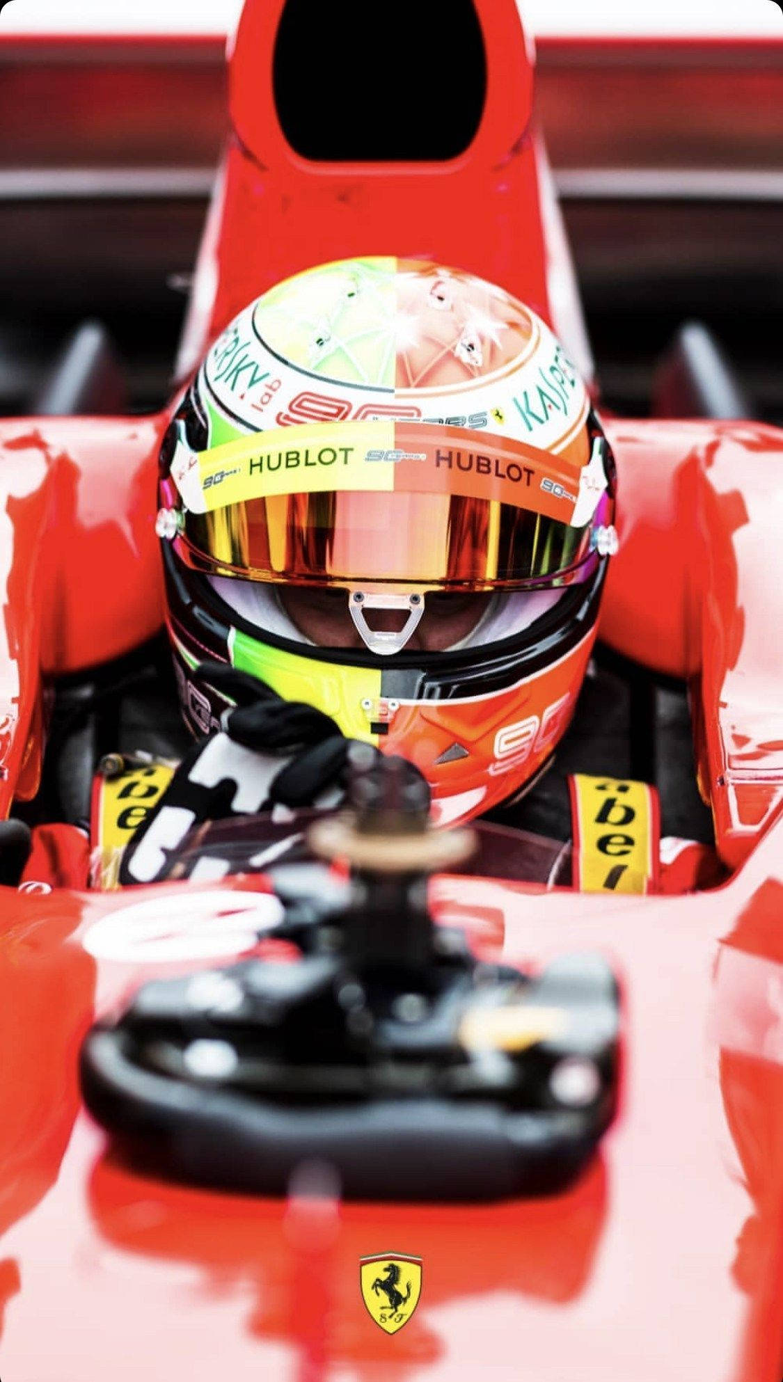 mick schumacher 桌布 壁紙 — 一級方程式車手在紅色法拉利駕駛艙內的近距離特寫，戴著帶有贊助商標誌的彩色頭盔。