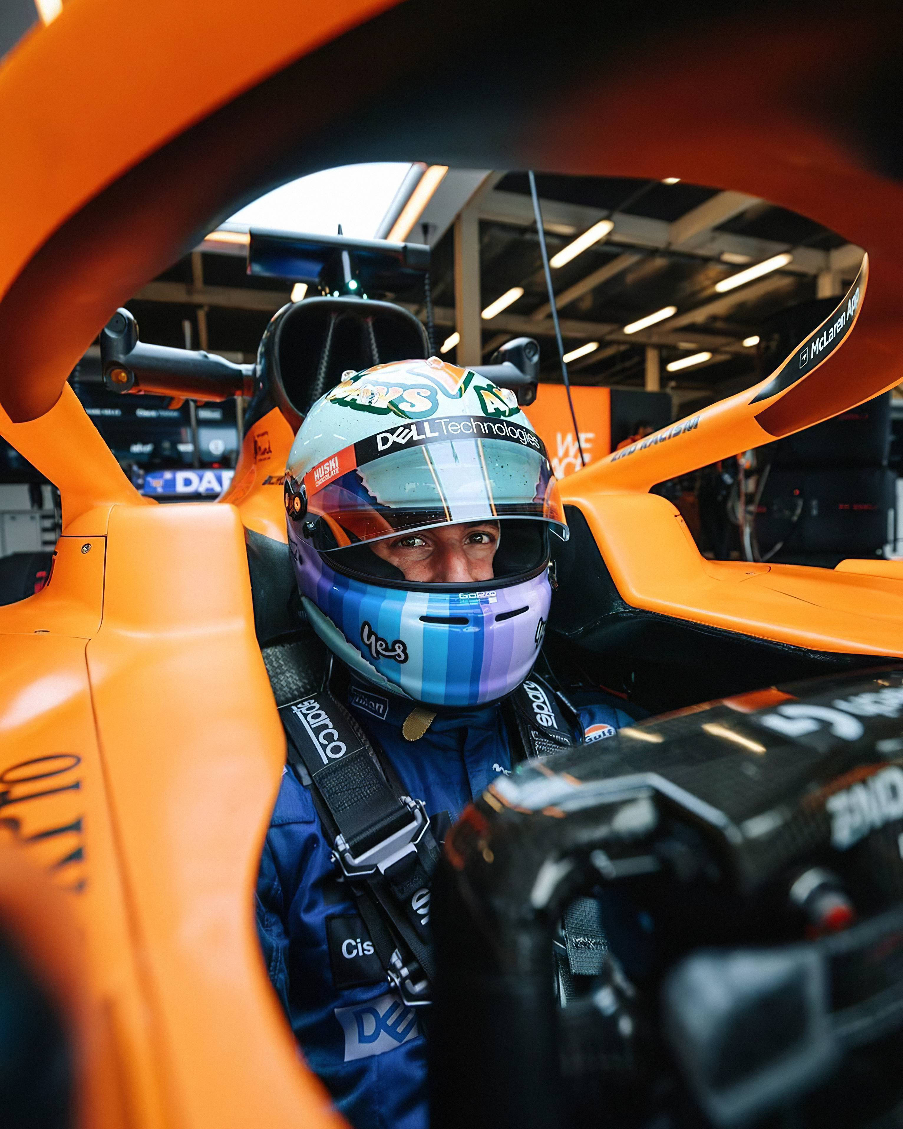 Racing 桌布 壁紙 — 一級方程式車手坐在充滿活力的橙色麥拉倫賽車駕駛艙內，戴著帶有贊助商標誌的彩色頭盔。