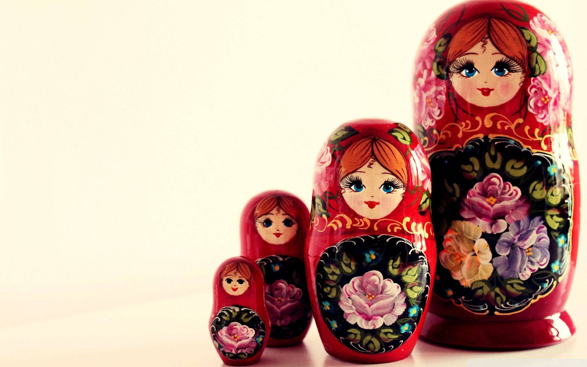 Russia 桌布 壁紙 — 一組四個精緻繪製的俄羅斯套娃，紅色身體帶有花卉圖案，按尺寸遞減排列在白色表面上。