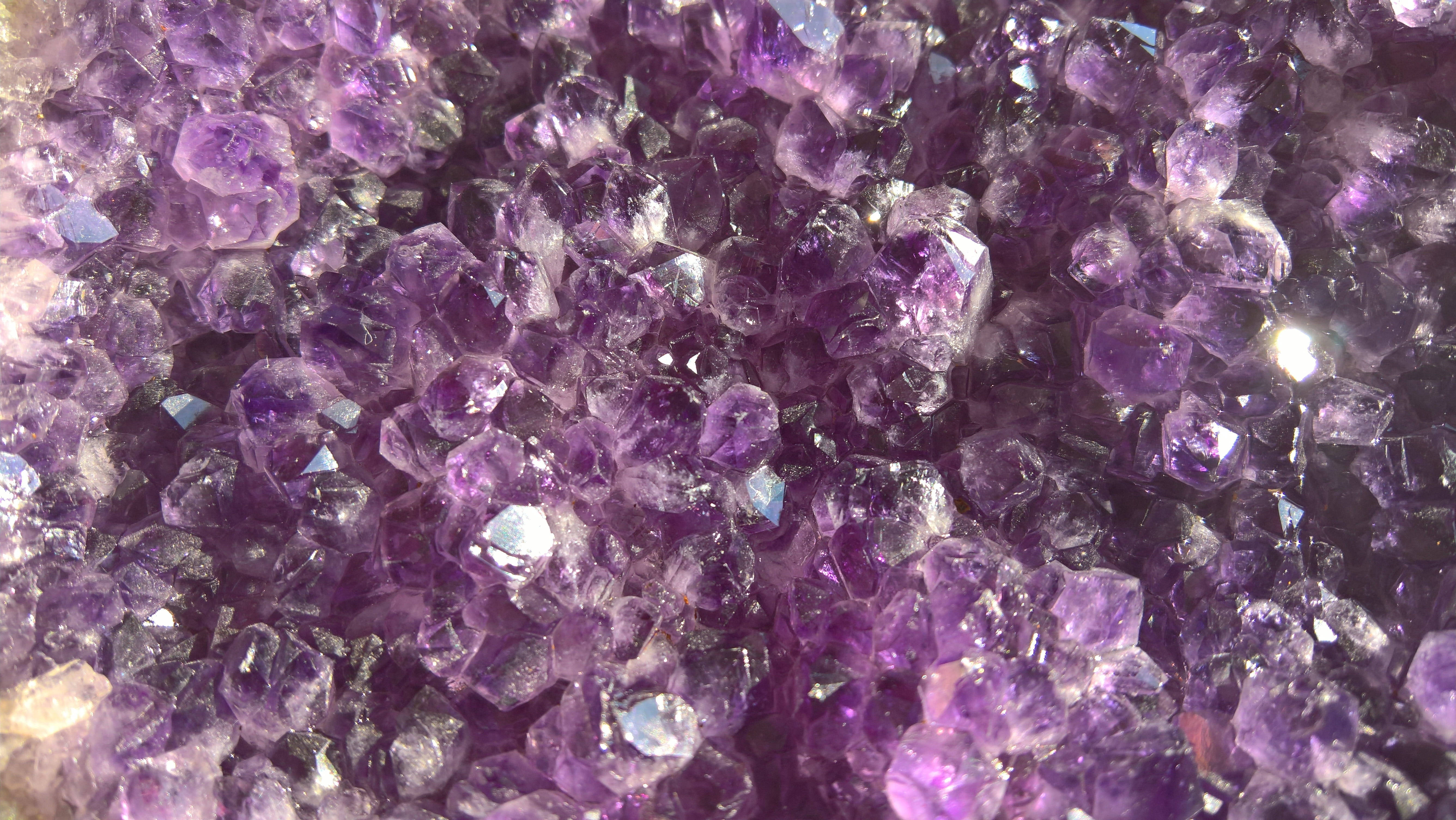 紫水晶 桌布 壁紙 — 一組密集的閃亮紫色紫水晶晶體特寫，其鋒利的刻面捕捉光線。