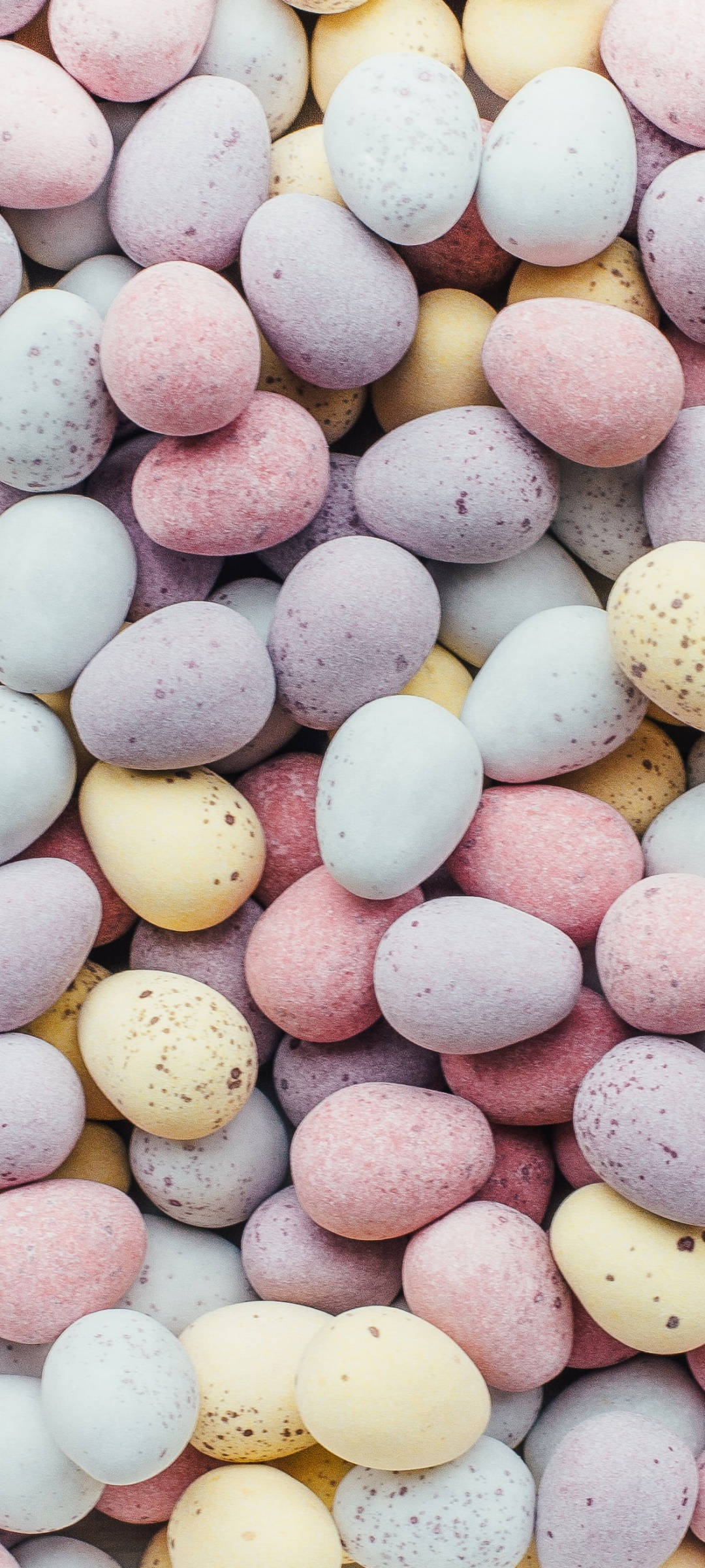 Aesthetic Easter 桌布 壁紙 — 一組柔和色調的粉彩色斑點巧克力蛋堆疊在一起的近距離特寫。