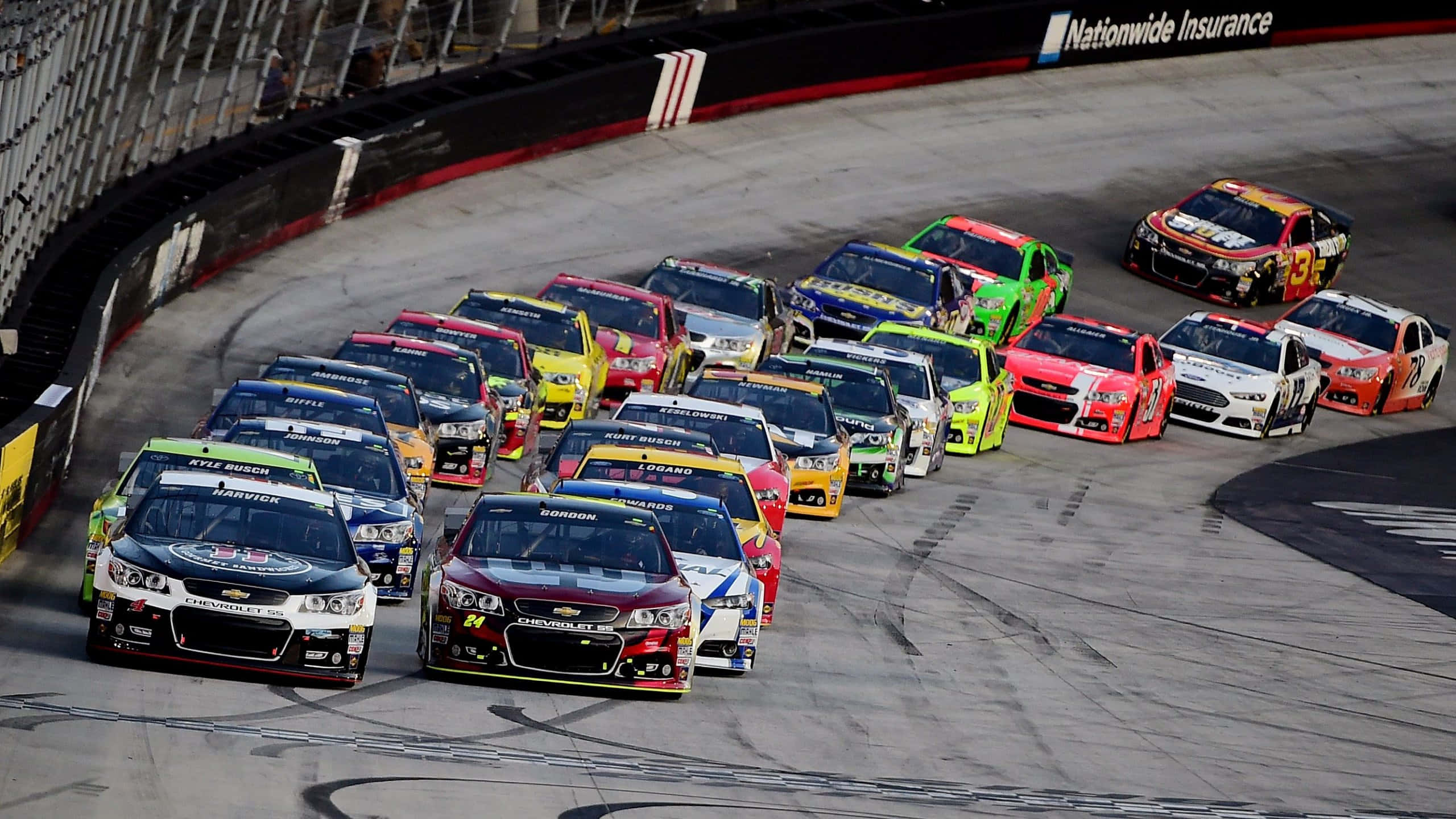 nascar 桌布 壁紙 — 一組色彩鮮豔的NASCAR賽車緊密地擠在一起，在賽道上高速過彎。