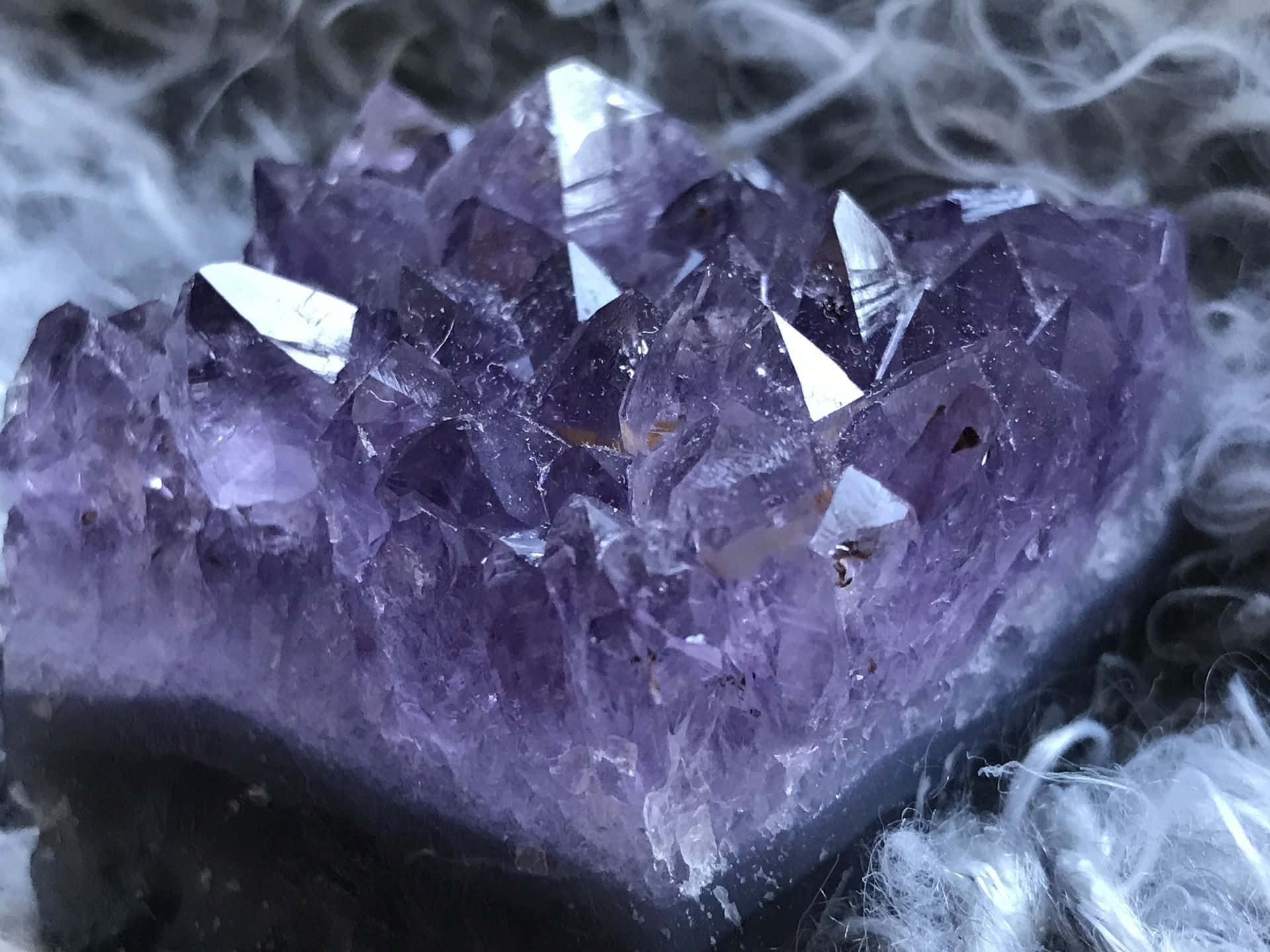 Amethyst 桌布 壁紙 — 一組閃閃發光的紫色紫水晶晶簇，周圍環繞著縷縷白煙的特寫。