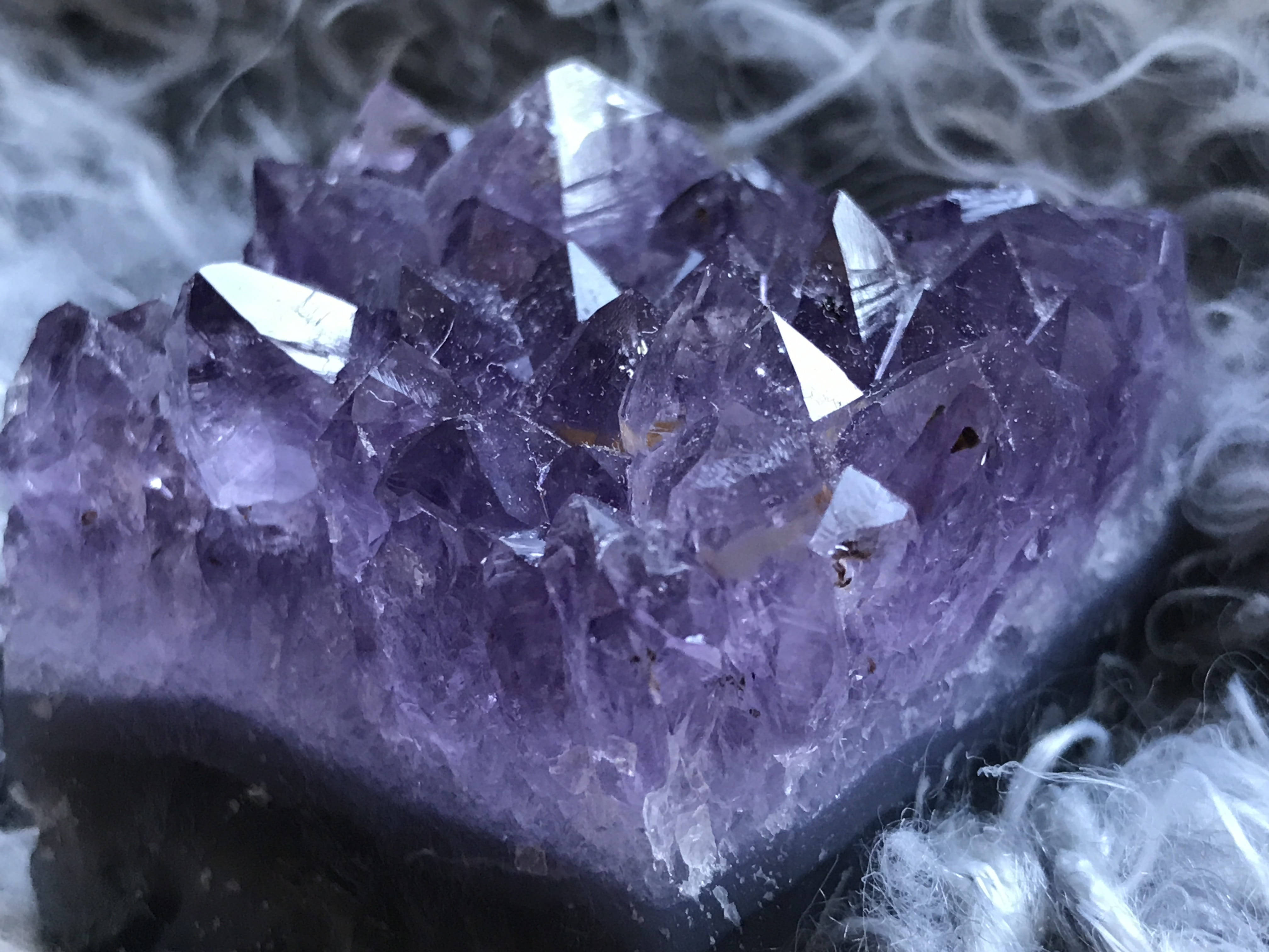 Amethyst 桌布 壁紙 — 一組閃閃發光的紫色紫水晶晶體簇的特寫，周圍環繞著旋轉的白煙。