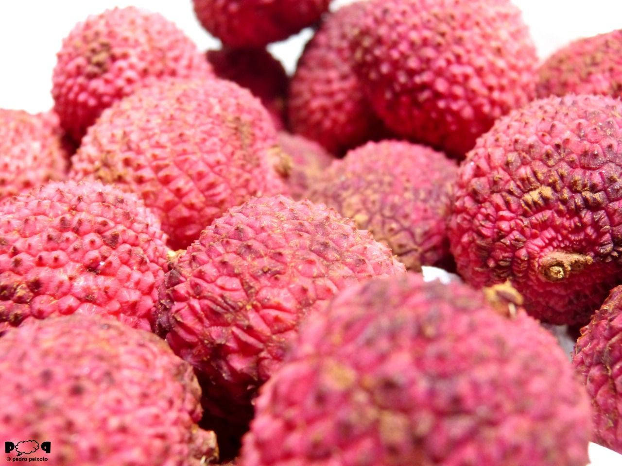 Fruits 桌布 壁紙 — 一組飽滿粉紅荔枝的特寫，表皮凹凸不平，堆疊在明亮的白色背景上。